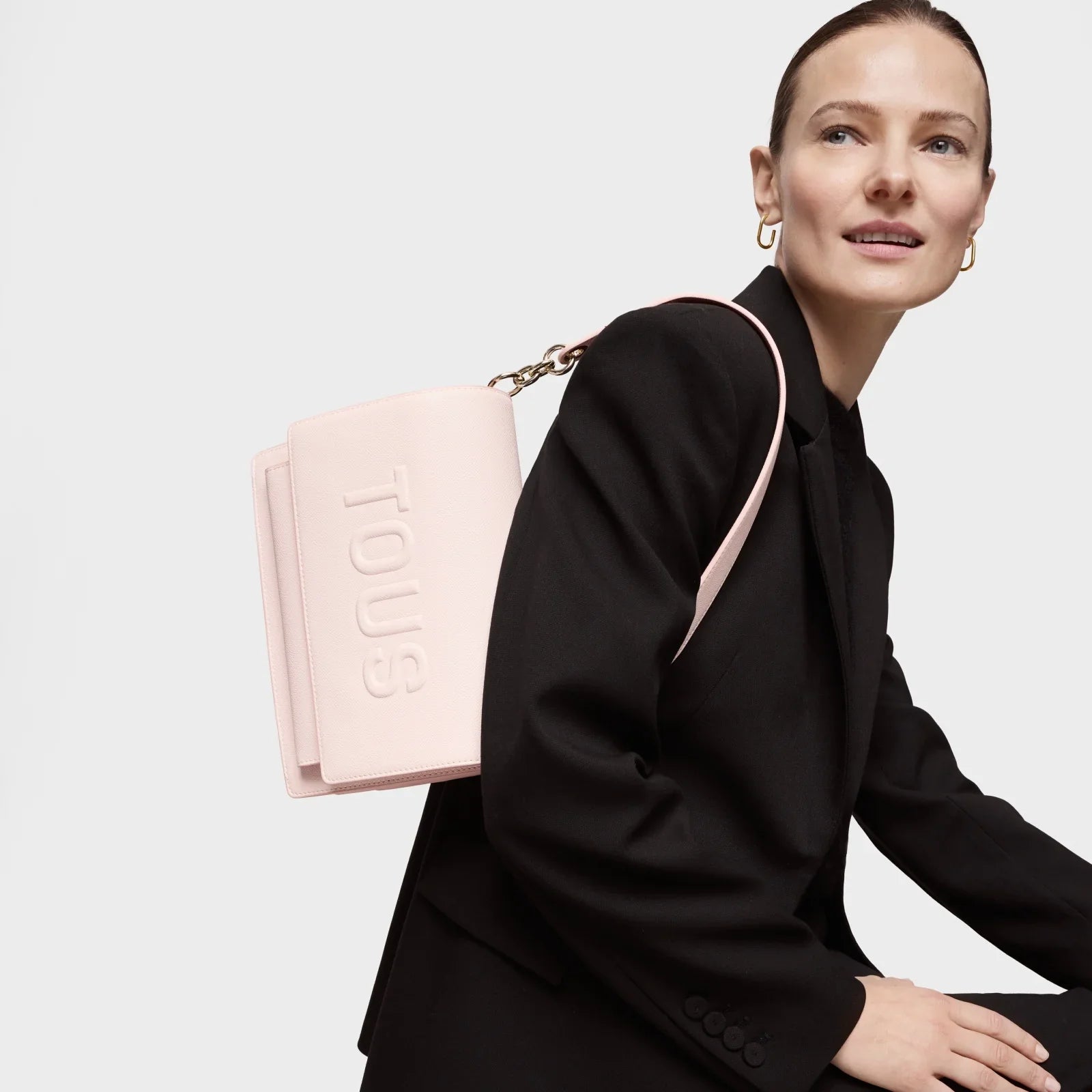 אישה לובשת חליפה שחורה עם תיק ורוד מבית TOUS, אופנה יוקרתית מקבוצת אלפא CHOZEN