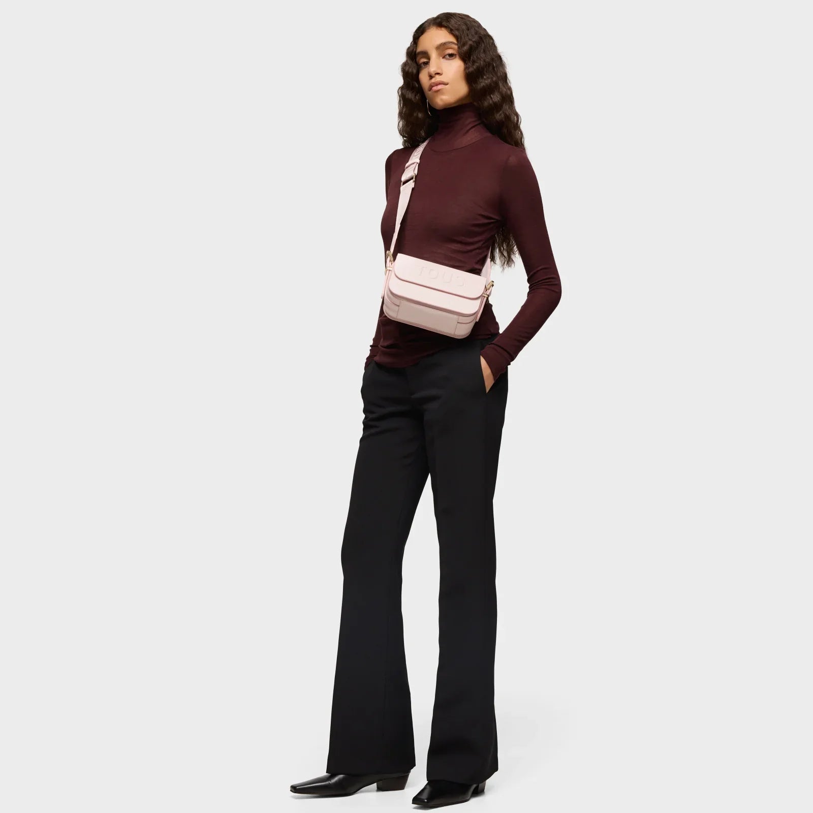 דוגמנית עם תיק צד ורוד של TOUS, חולצת גולף יין ומכנסיים שחורים, צילום לאתר CHOZEN