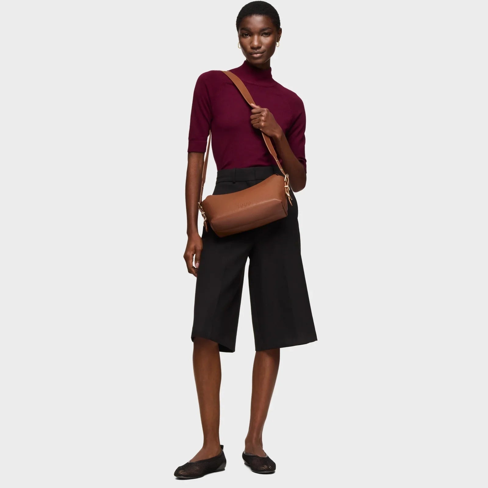 דוגמנית מחזיקה תיק עור חום עם רצועת צד, חולצת בורדו ומכנסיים שחורים, מותגים מובילים ב-CHOZEN