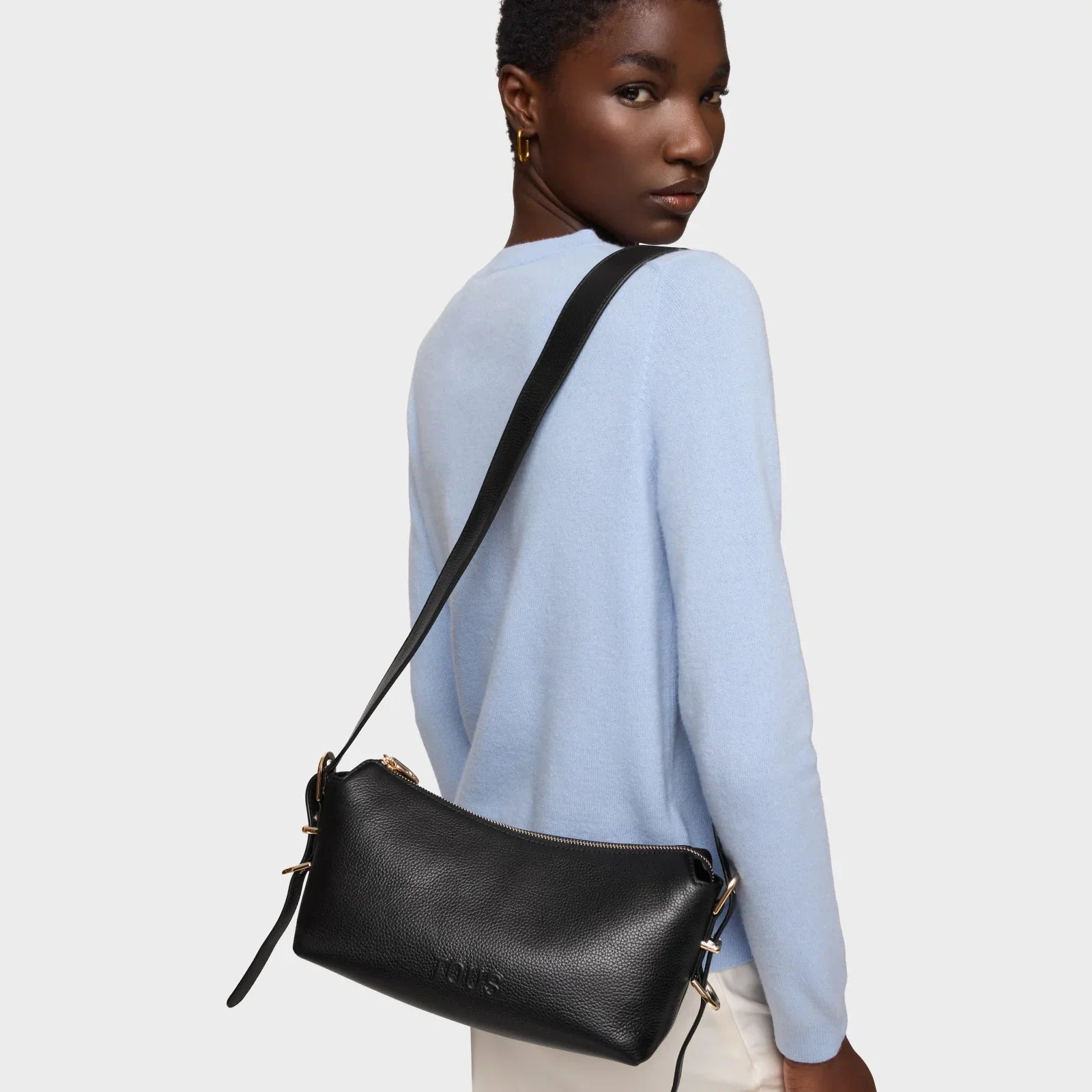 אישה עם תיק צד שחור מעור של TOUS, לבושה סוודר תכלת אופנתי, מבית CHOZEN