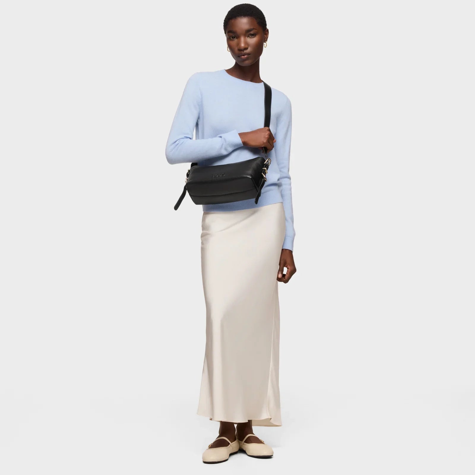 דוגמנית עם סוודר תכלת, חצאית לבנה, תיק שחור וסטייל אלגנטי מתוך מותגי CHOZEN