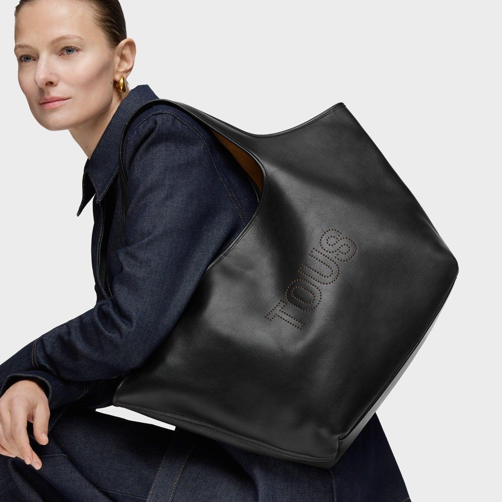 אישה לובשת ג'ינס נושאת תיק עור שחור TOUS, מותג אופנה יוקרתי באתר CHOZEN