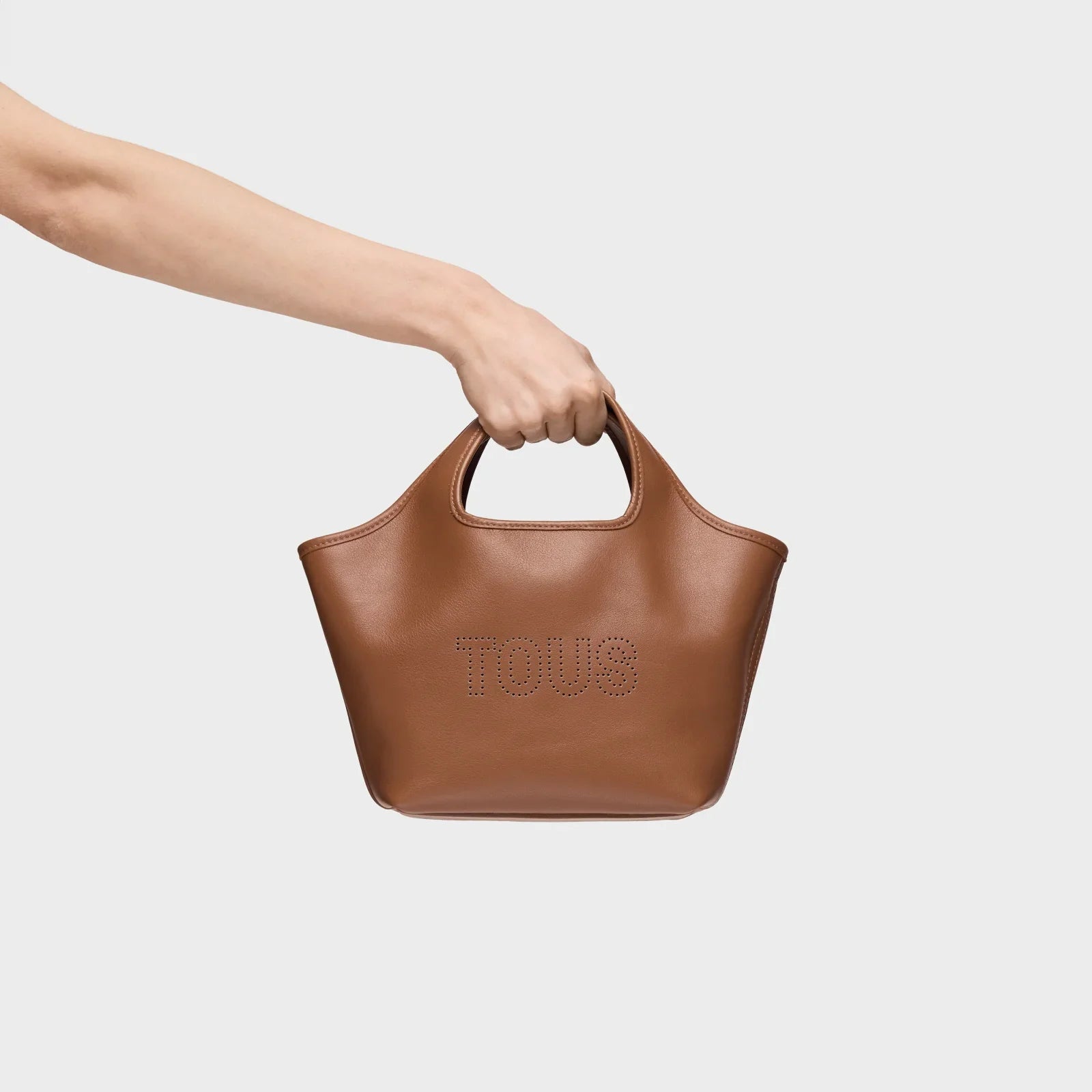 תיק עור חום של TOUS ביד על רקע לבן, מותג מוביל באתר CHOZEN
