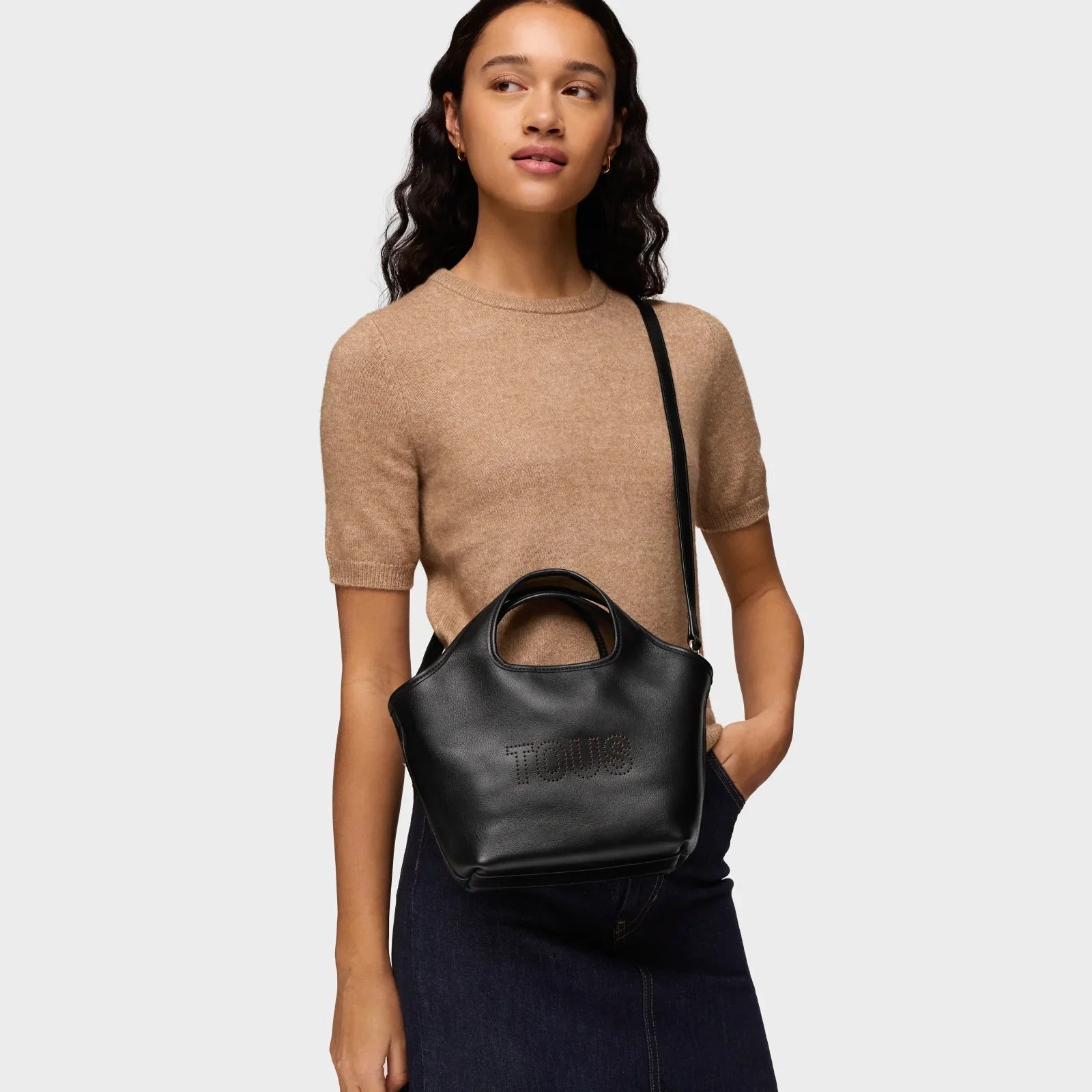 אישה עם תיק צד עור שחור TOUS מבית קבוצת אלפא, חולצה בז' וחצאית ג'ינס