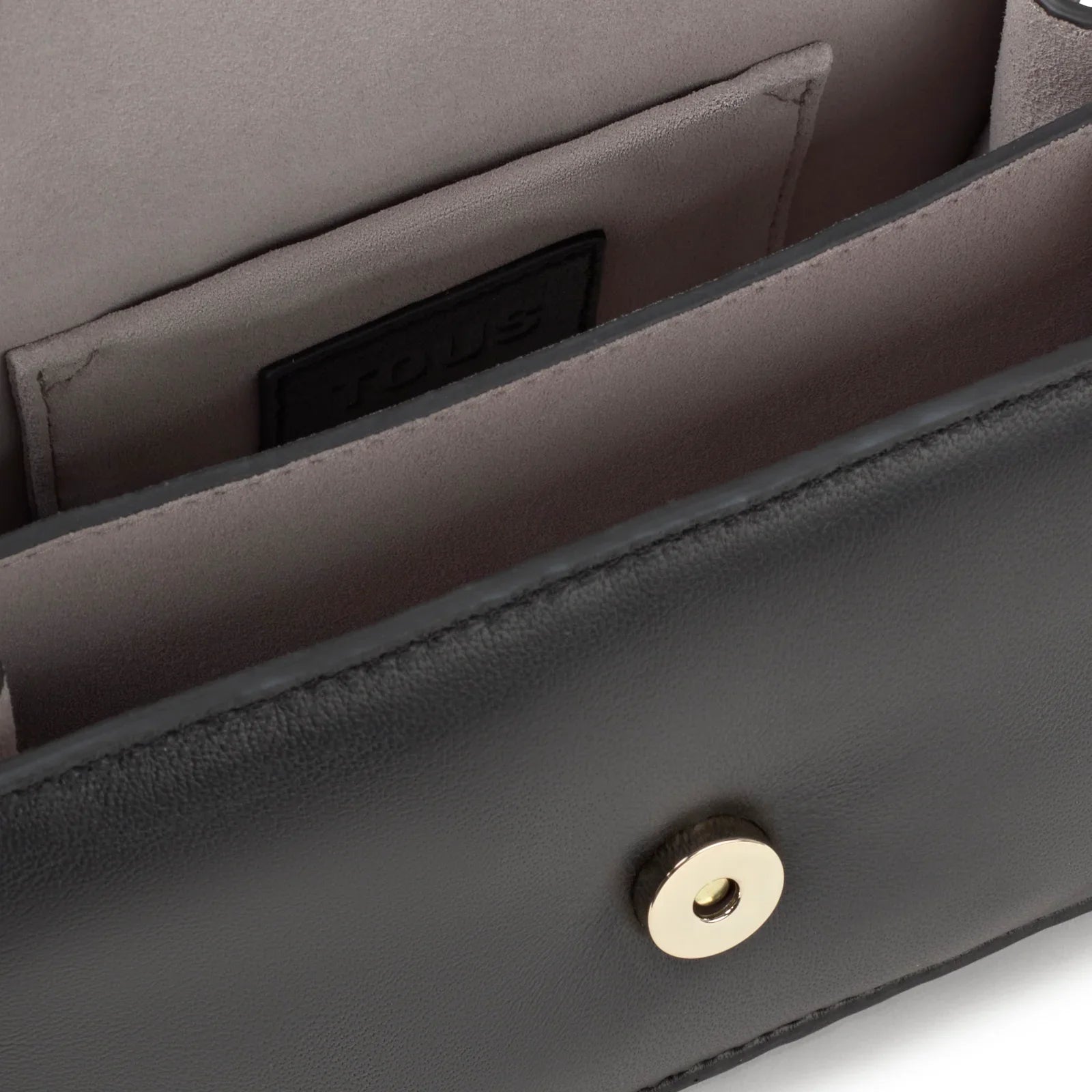 קלוז-אפ של פנים תיק עור שחור יוקרתי עם ריפוד פנימי וכפתור מתכת בחזית, מיתוג TOUS