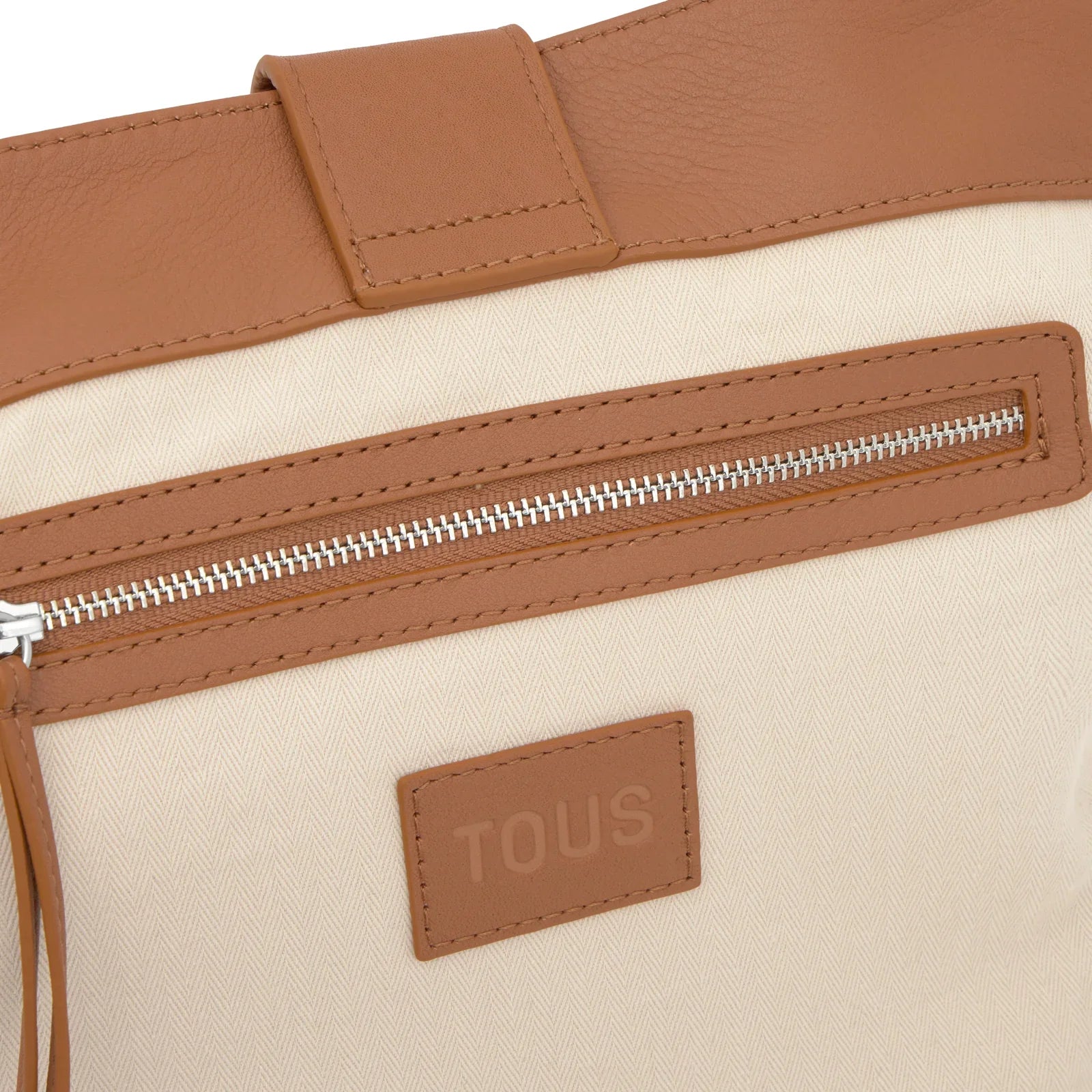 תקריב של תיק בעיצוב אלגנטי בצבע בז' וחום עם רוכסן ולוגו TOUS, מותג יוקרה ב-CHOZEN