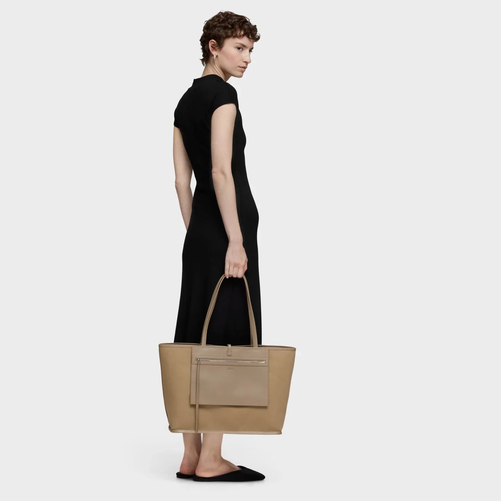 אישה בשמלה שחורה מחזיקה תיק יד בז׳, אופנה יוקרתית CHOZEN קבוצת אלפא