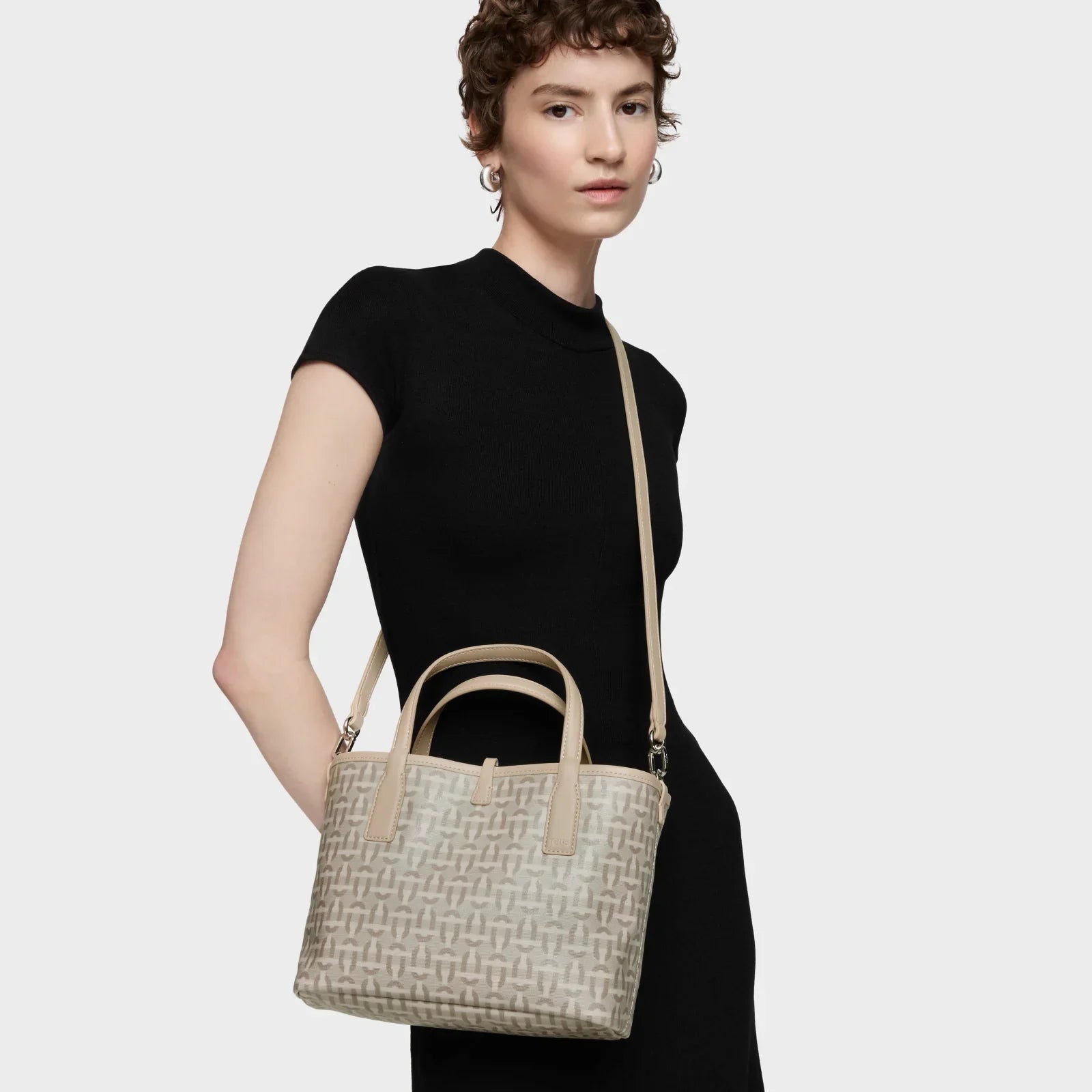 דוגמנית עם שמלה שחורה מחזיקה תיק יד אופנתי בז׳ עם דוגמת לוגו, CHOZEN מותגים מובילים