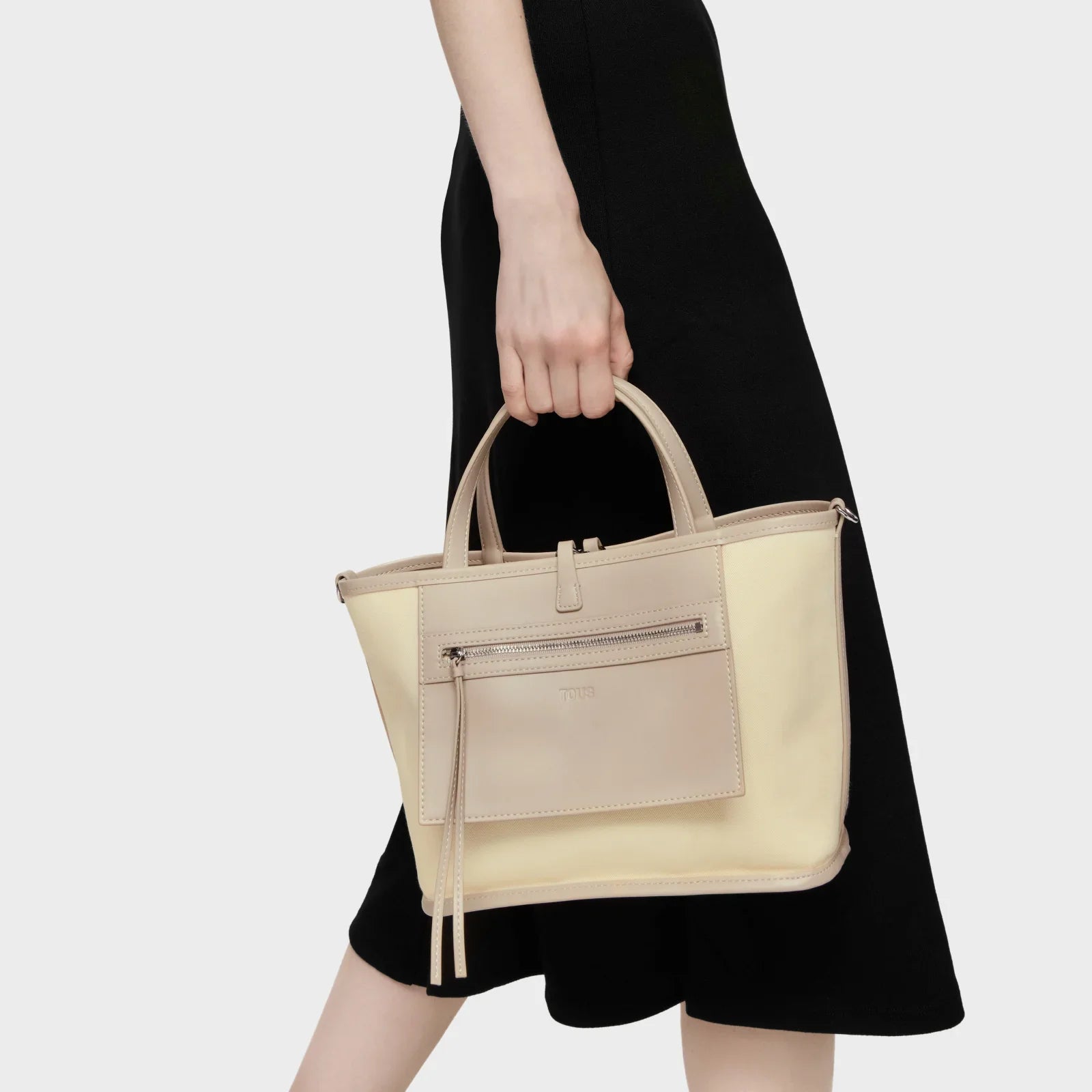 אישה בשמלה שחורה מחזיקה תיק יד אלגנטי בגוון בז' מבית CHOZEN