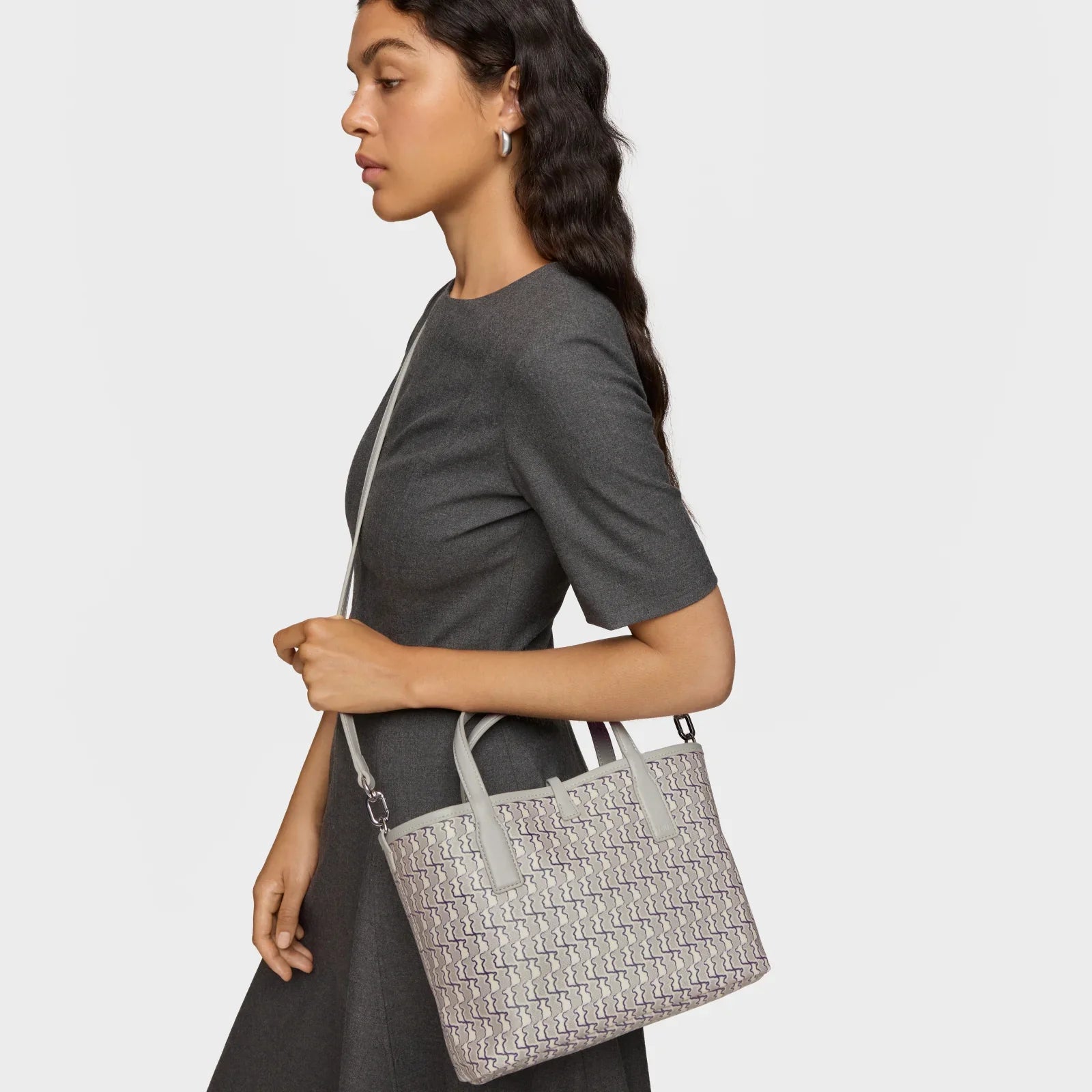 אישה לובשת שמלה אפורה ונושאת תיק יד אופנתי מבית CHOZEN, רקע לבן