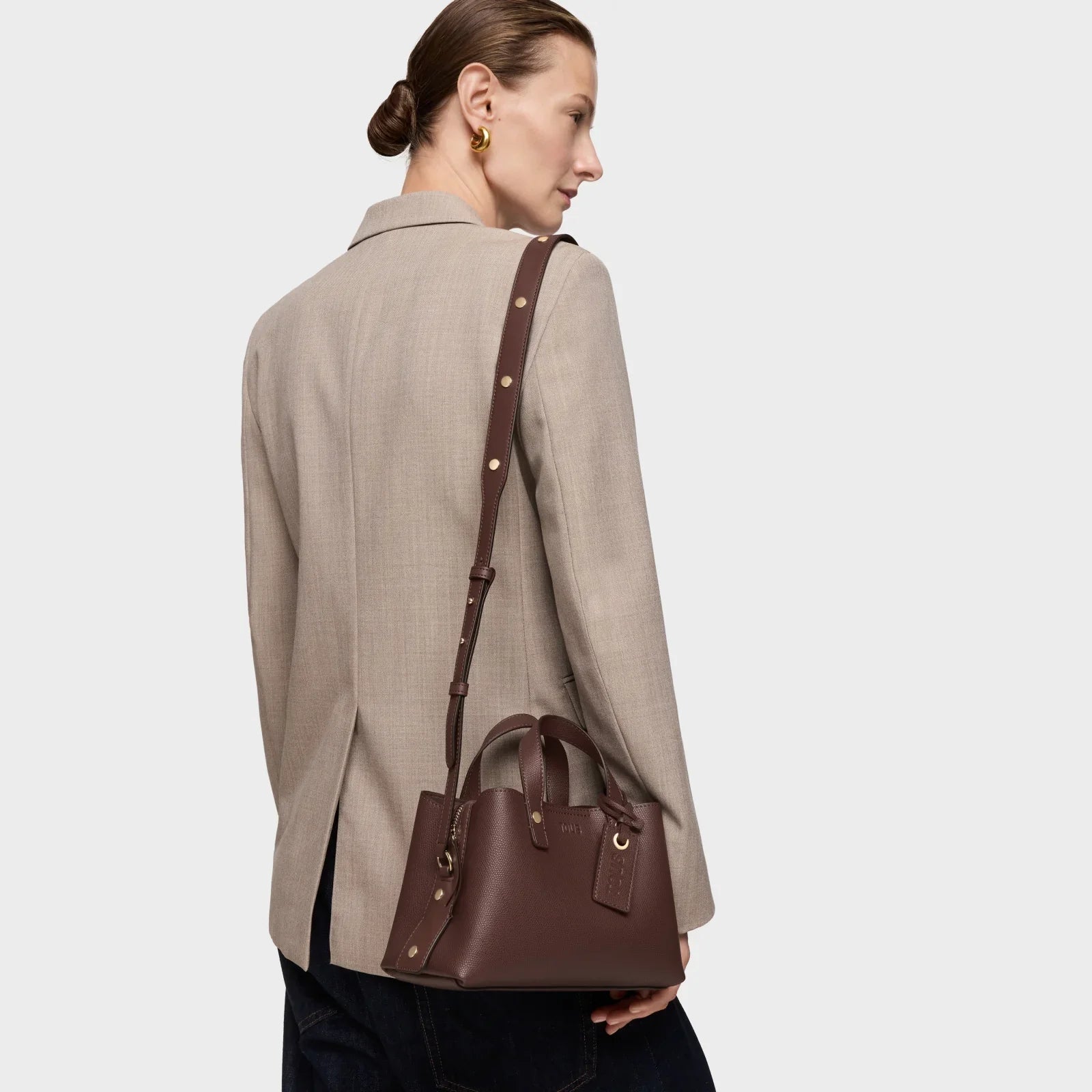 אישה עם תיק עור חום מעוצב על כתף, בחליפה אלגנטית, צולם ל-CHOZEN מותגים מובילים