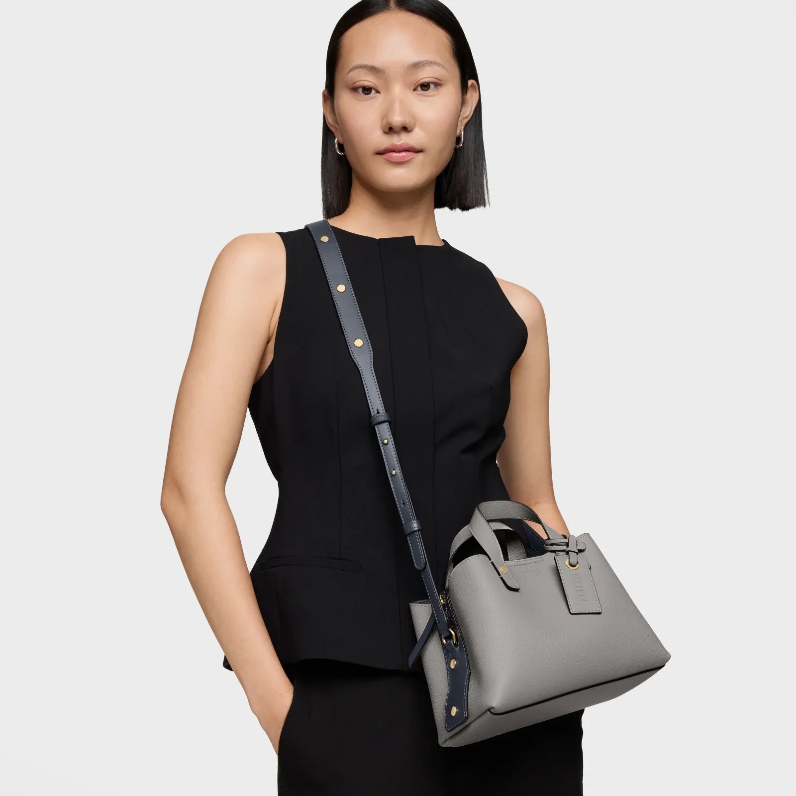 אישה לובשת שמלה שחורה אלגנטית ומחזיקה תיק יד אפור, אופנה יוקרתית מבית CHOZEN