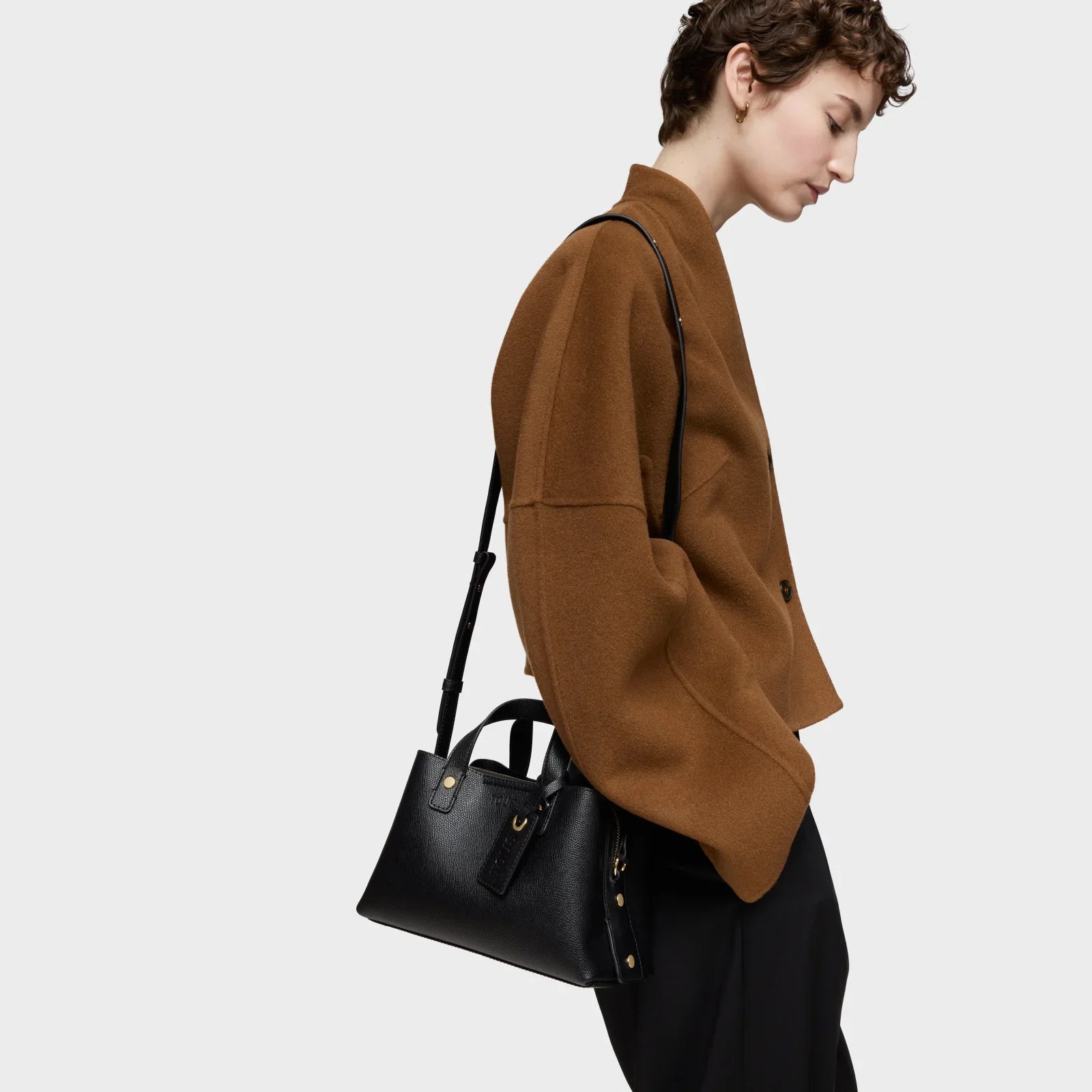 אישה עם תיק מעוצב שחור על כתף, לובשת ג'קט חום אופנתי, צילום סטודיו לאופנה CHOZEN