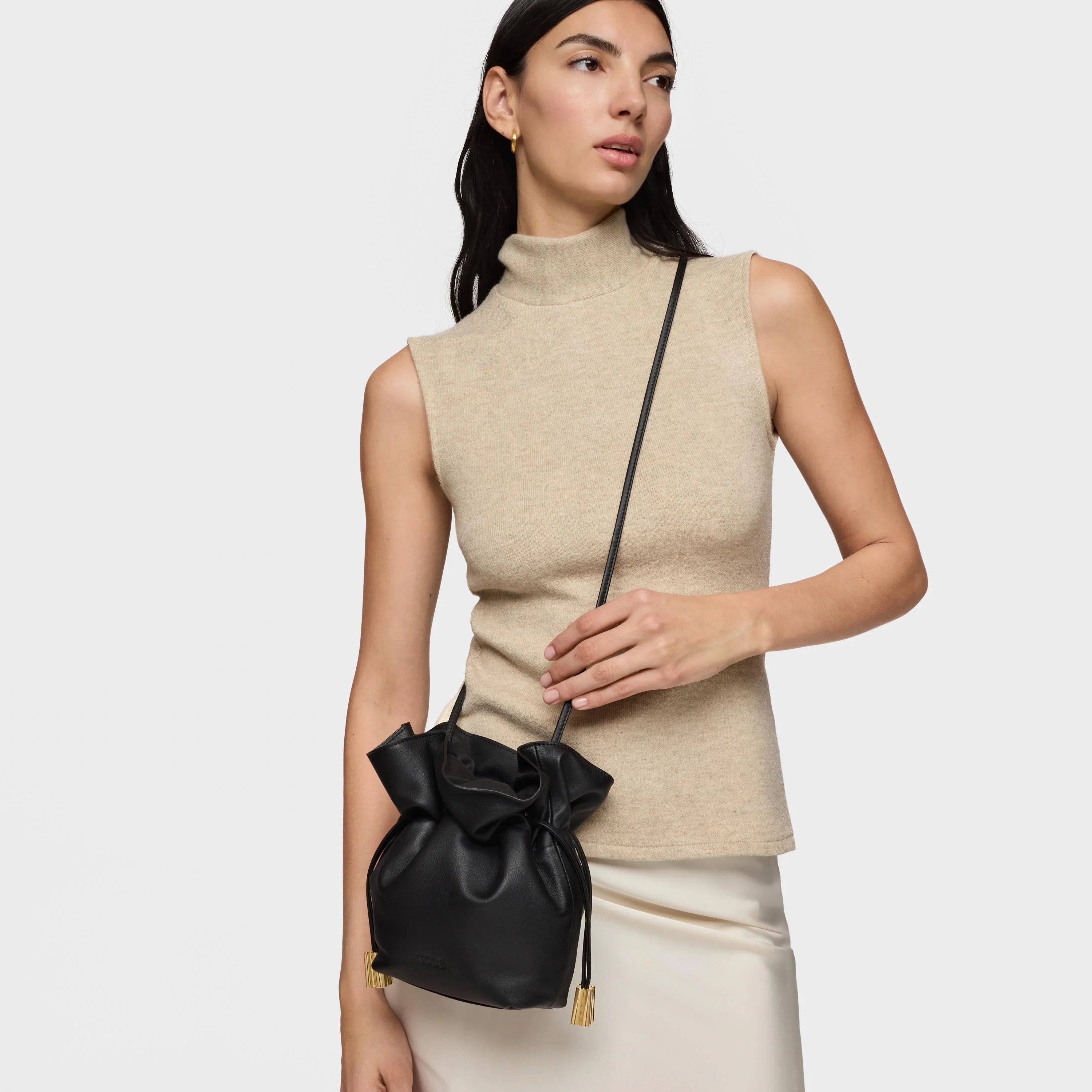 דוגמנית עם תיק עור שחור קטן בעיצוב שק, לבושה בגופיית צווארון גולף בז'