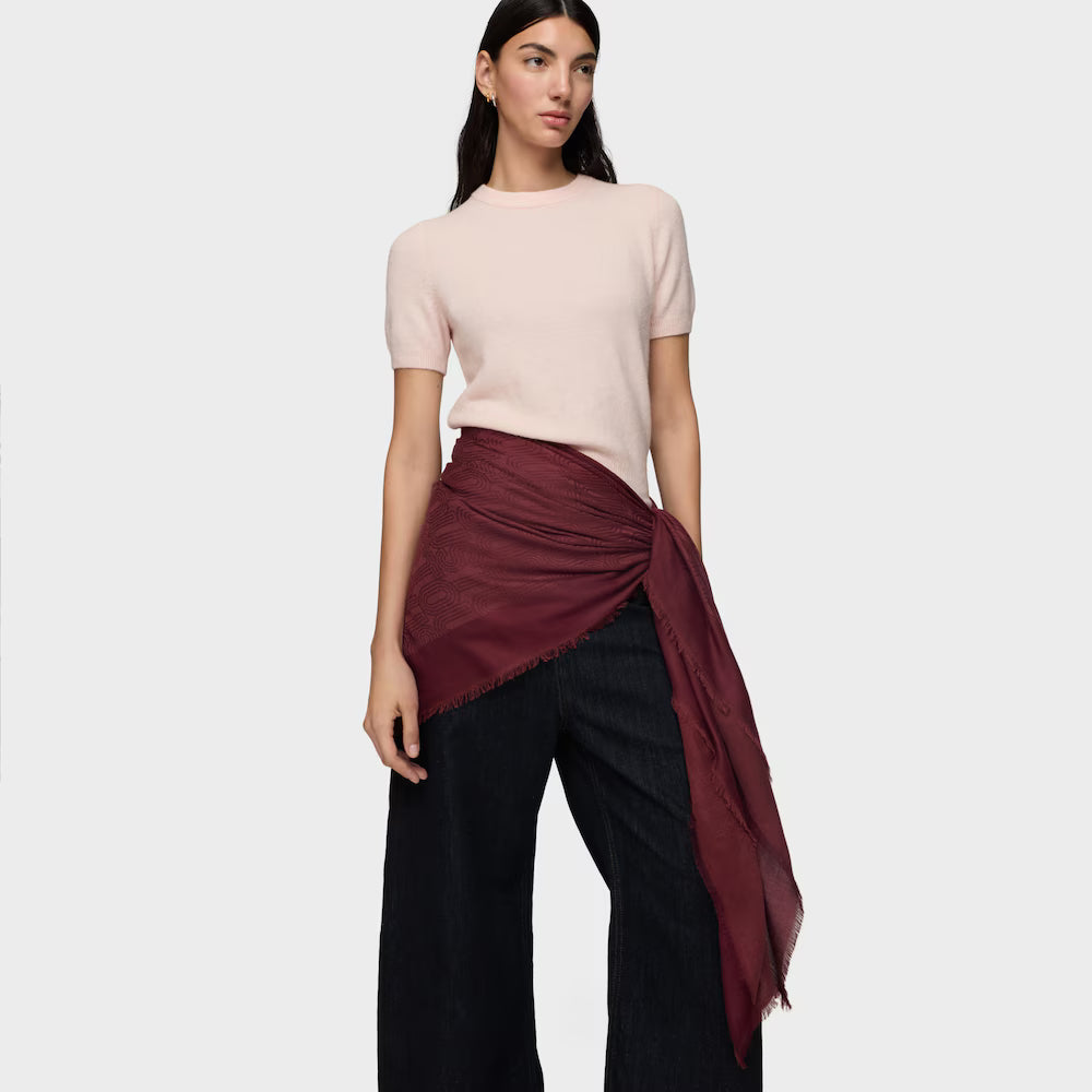 אישה עם חולצה בהירה, צעיף בורדו ומכנסיים רחבים שחורים לאופנה אלגנטית