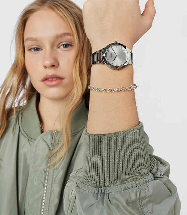 אישה לובשת מעיל ירוק, מציגה שעון יד כסוף וצמיד כסף, צילום אופנה ל-CHOZEN