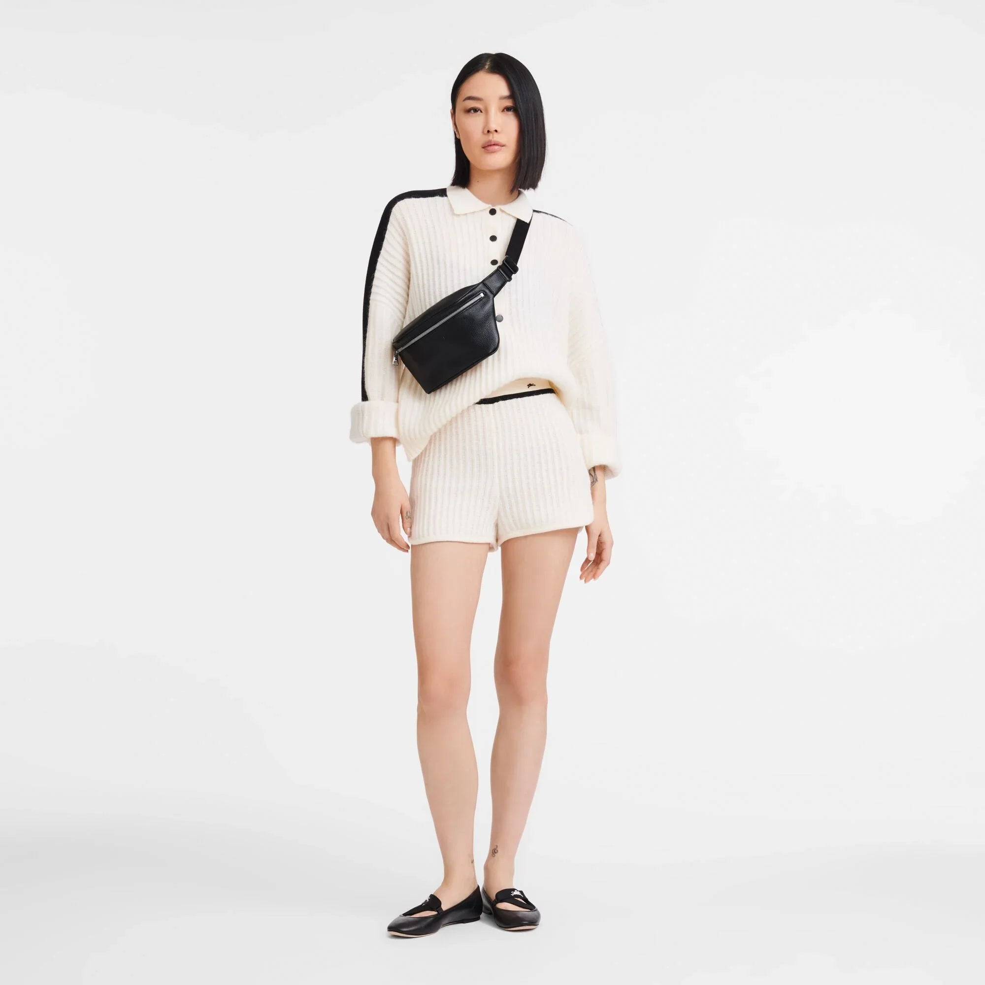 אישה לובשת חולצת וסריג קצרה בצבע שמנת, תיק צד שחור ונעליים שחורות, צילום אופנה CHOZEN