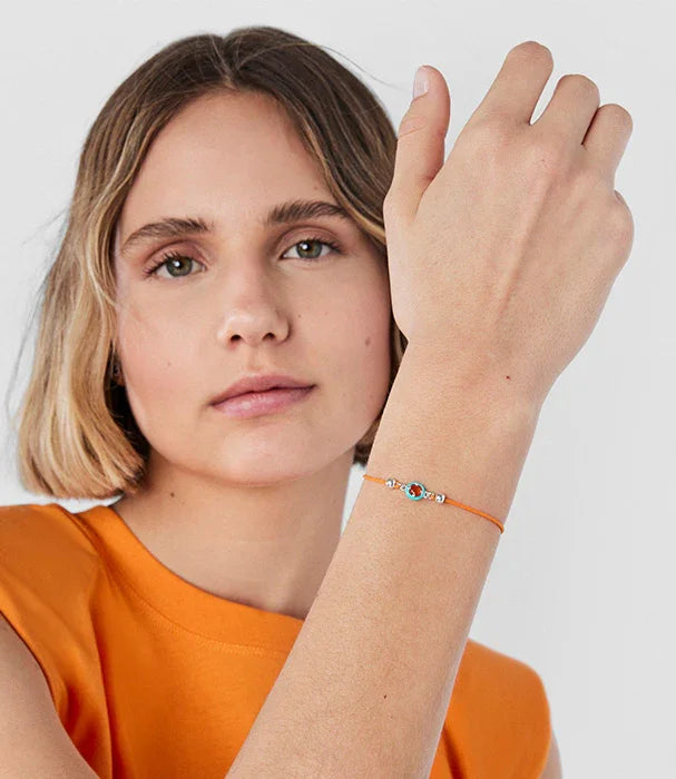 אישה לובשת חולצה כתומה וצמיד עדין עם חוט כתום ותליון עין, צילום ל-CHOZEN מותגים מובילים