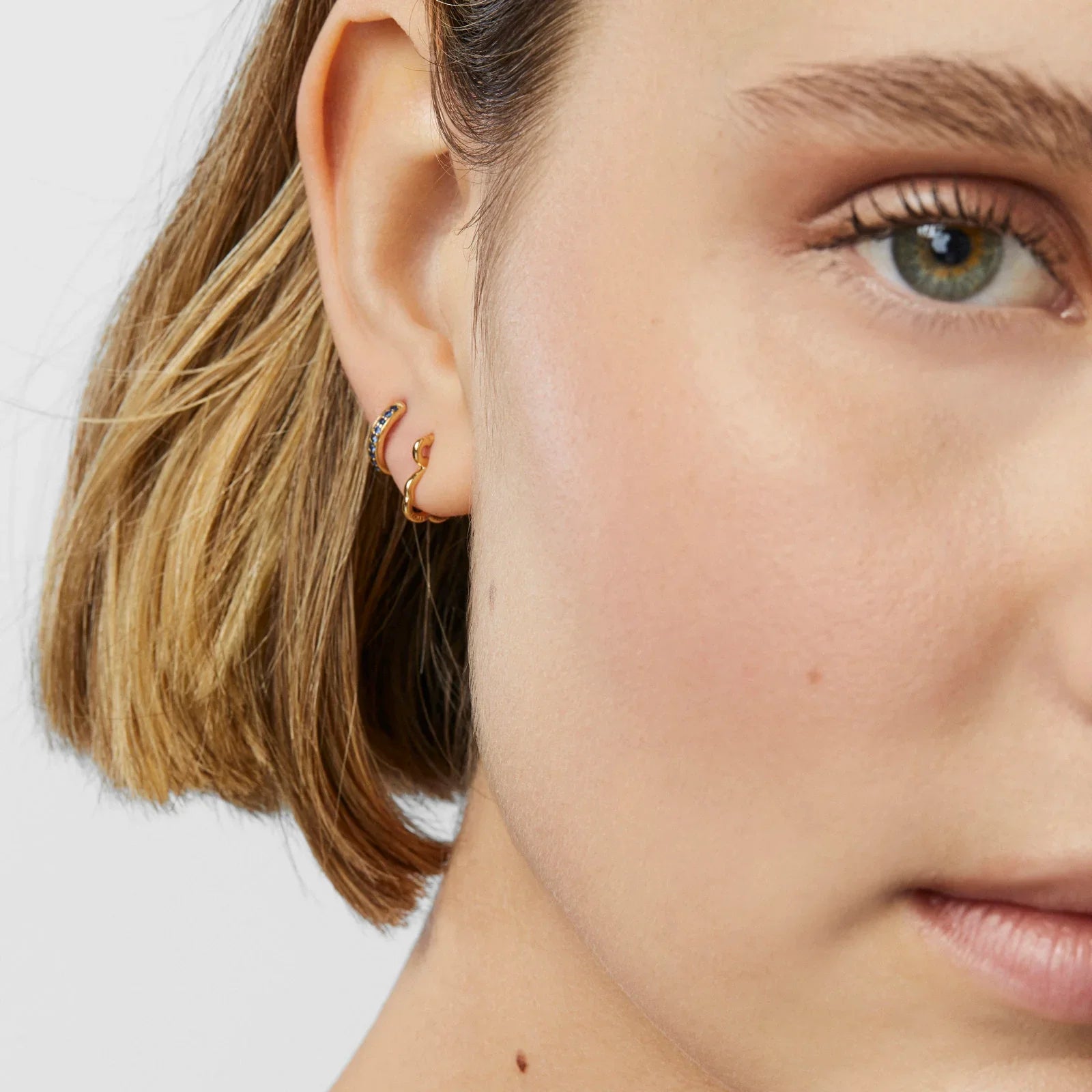 עגילי זהב מעוצבים עם אבני חן על אוזן אישה, צילום תקריב ממותגי CHOZEN