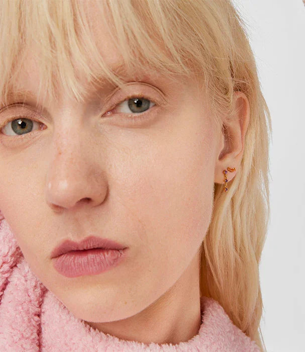 אישה בלונדינית עם עגיל זהב צבעוני, לבושה בסוודר ורוד, אופנה מבית CHOZEN