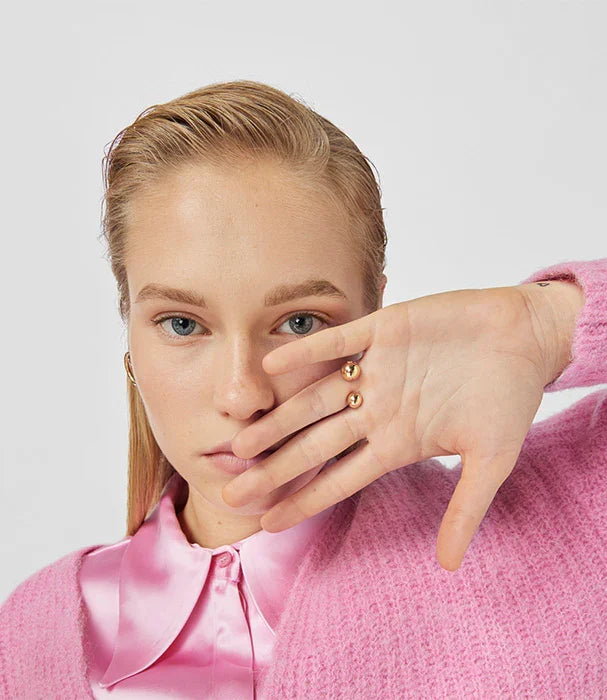 אישה במעיל ורוד עם חולצת סאטן ורודה, עונדת טבעת זהב טרנדית, CHOZEN מותגים מובילים