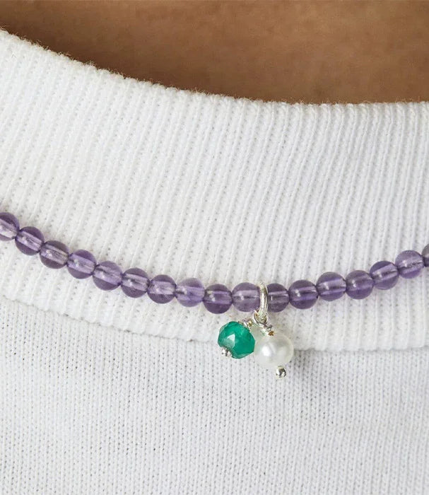 שרשרת חרוזים סגולים עם תליון ירוק ולבן מבית CHOZEN על רקע חולצה לבנה