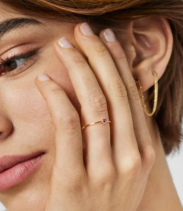 תקריב של אישה עונדת טבעת זהב עדינה עם אבן סגולה ועגילי זהב, תכשיטי אופנה יוקרתיים ב-CHOZEN