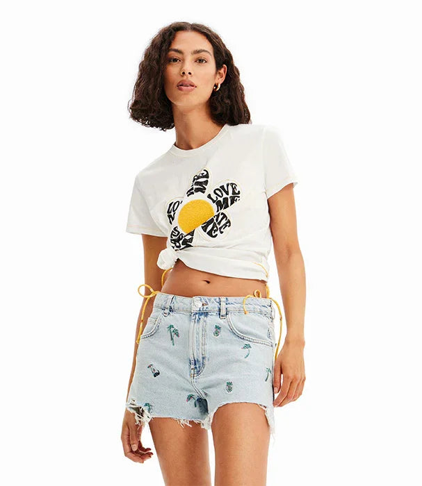 אישה לובשת חולצת טי לבנה עם פרח וכיתוב LOVE ME ומכנסי ג'ינס קצרים עם הדפסי אננס, אופנת קיץ CHOZEN