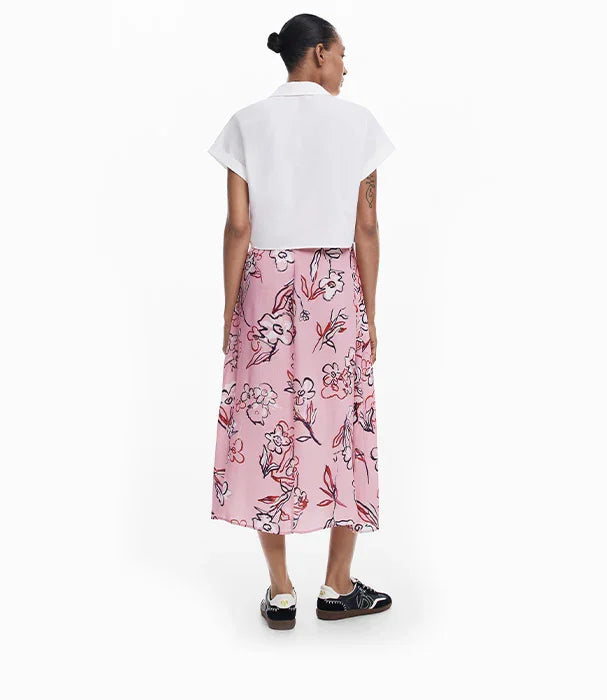 אישה לובשת חולצה לבנה קצרה וחצאית ורודה עם הדפס פרחוני מבית CHOZEN