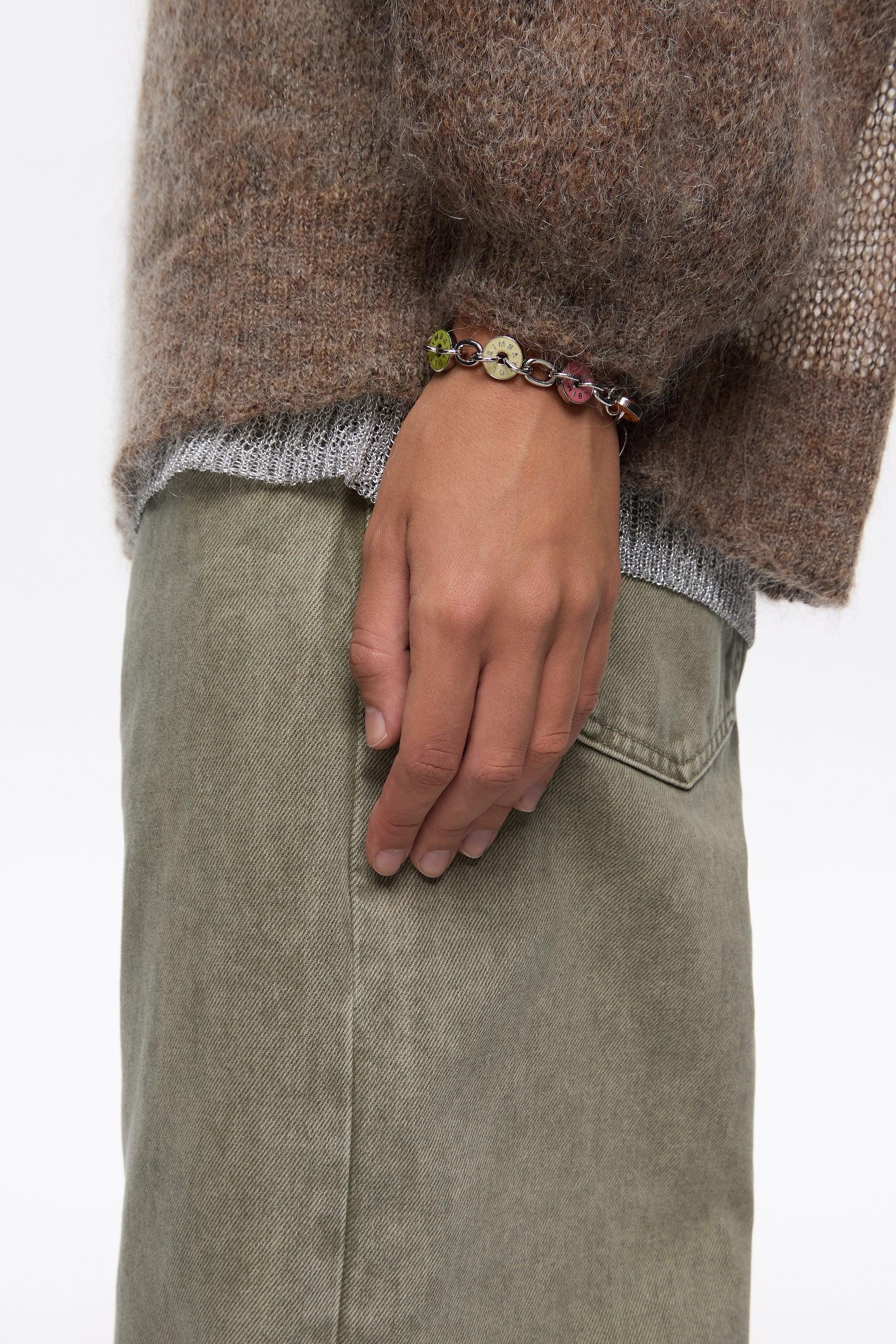 יד עונדת צמיד עגולים צבעוניים, סוודר חום ומכנס ירוק, אופנה CHOZEN