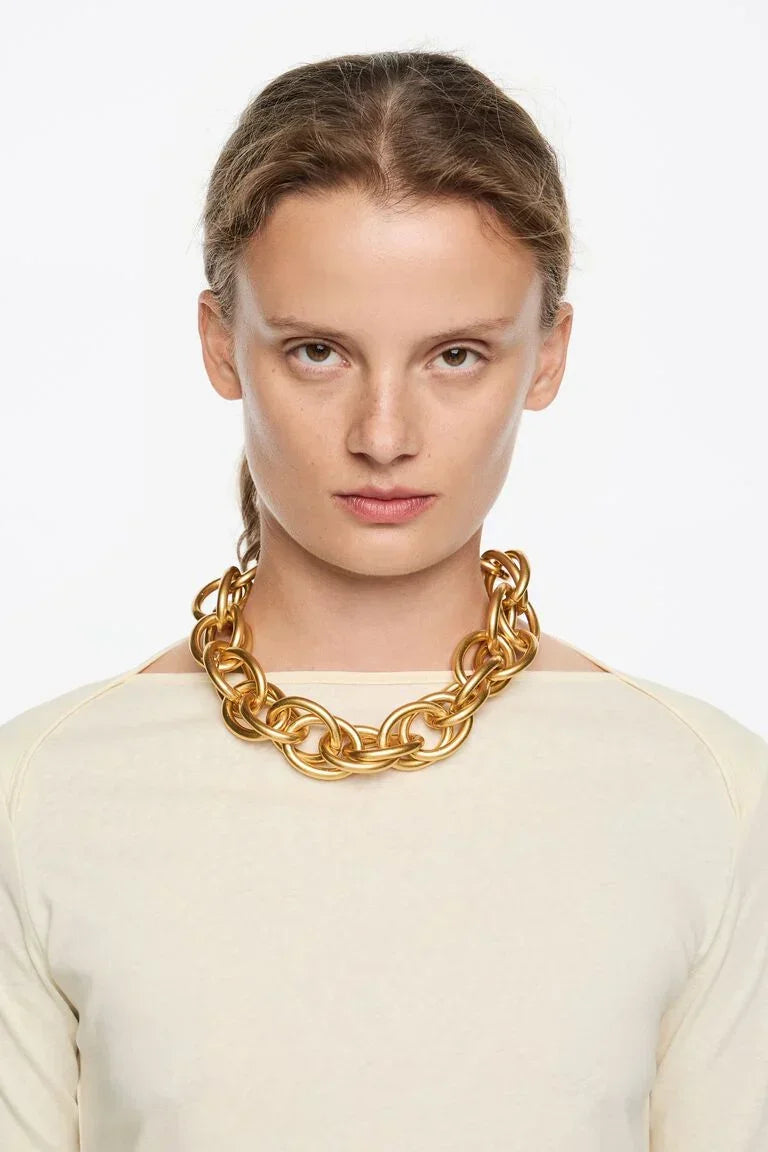 דוגמנית עם שרשרת זהב עבה, חולצה בהירה, רקע לבן – תכשיטים יוקרתיים CHOZEN