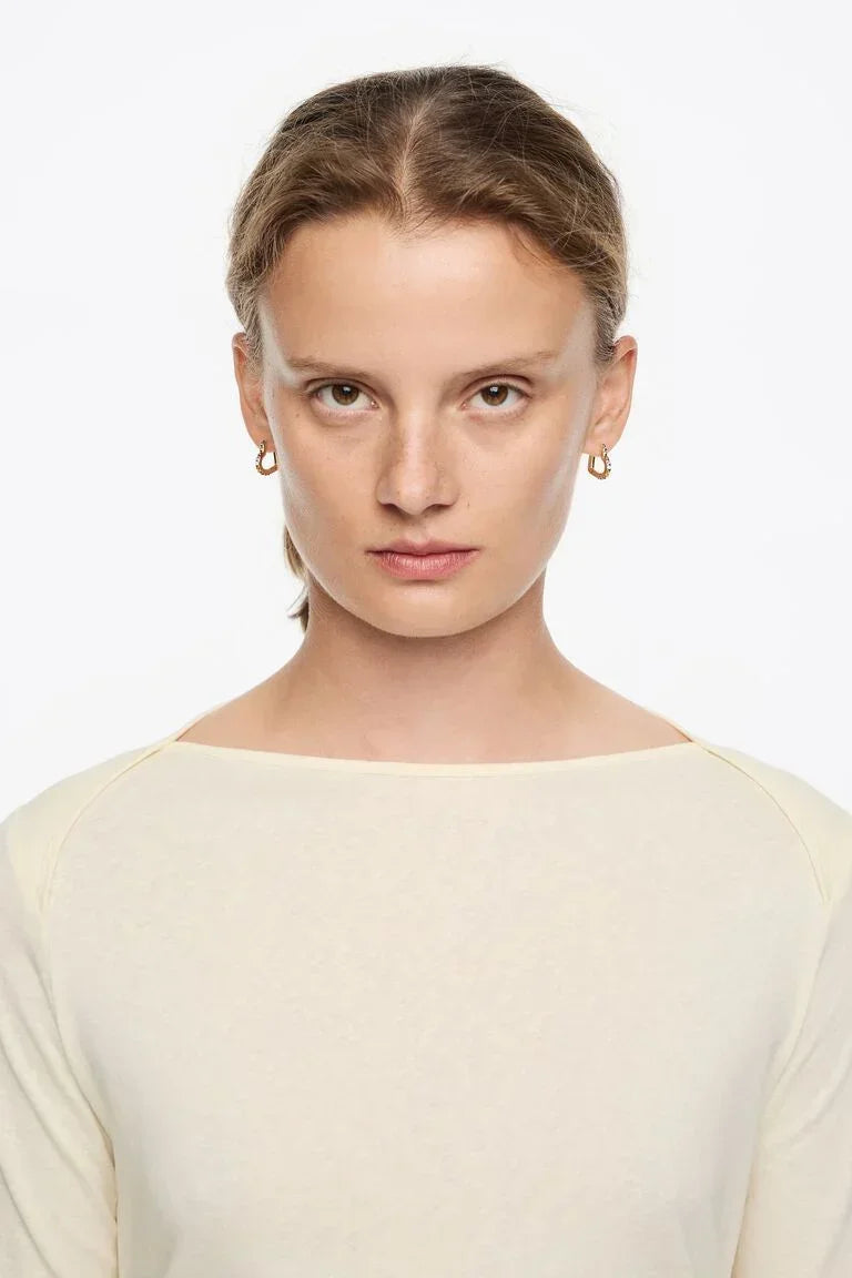 דוגמנית עם שיער אסוף, עונדת עגילי זהב בחולצת בז', צילום סטודיו לאופנה CHOZEN