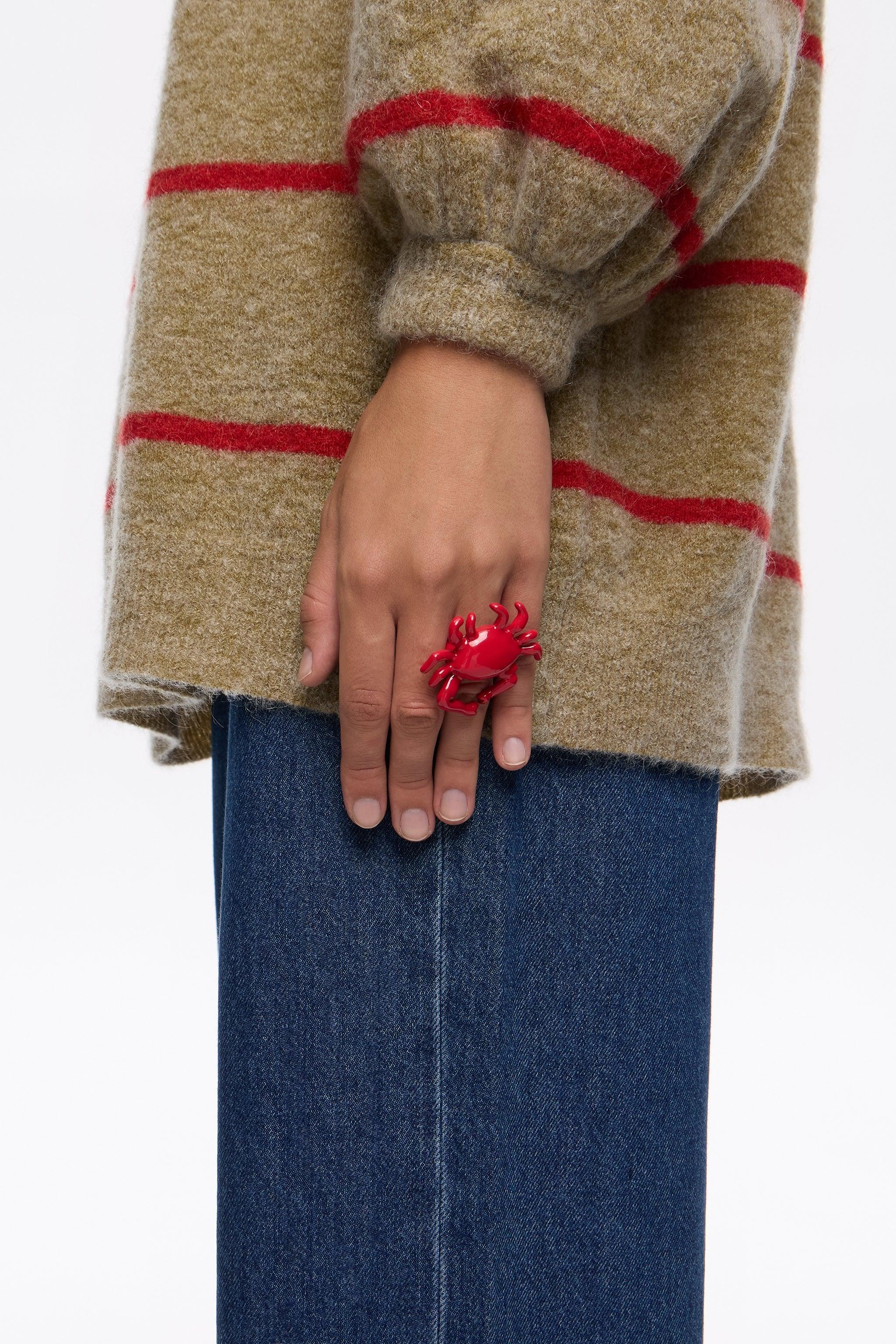 אצבע עם טבעת סרטן אדומה, סוודר פסים בז' עם אדום וג'ינס, קולקציה של CHOZEN