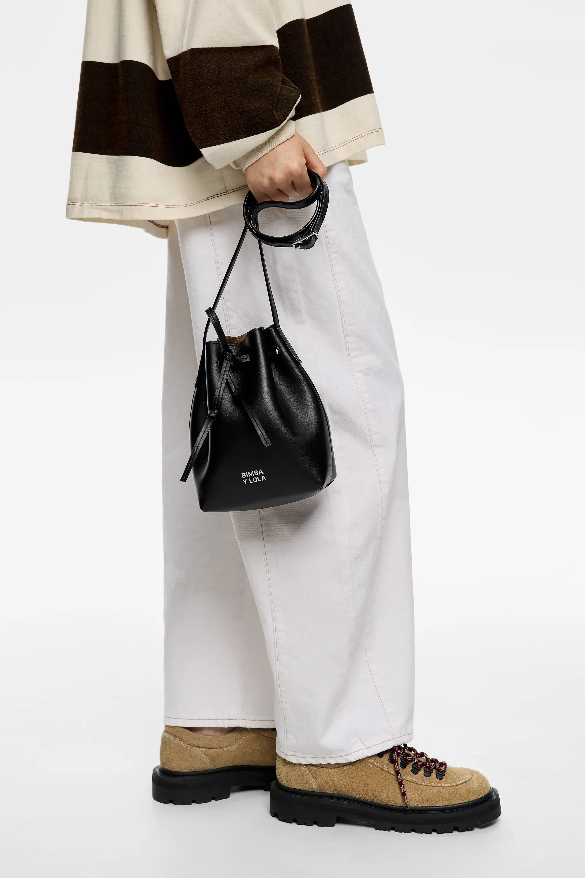 תיק שק קטן שחור של BIMBA Y LOLA ביד, עם מכנסיים לבנים ונעליים בז', קבוצת אלפא CHOZEN