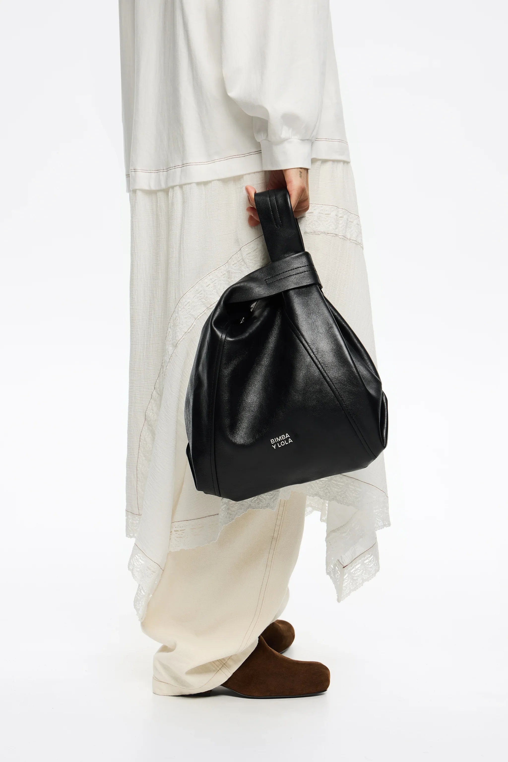 תיק עור שחור של BIMBA Y LOLA ביד דוגמנית עם שמלה לבנה, אופנה יוקרתית ב-CHOZEN