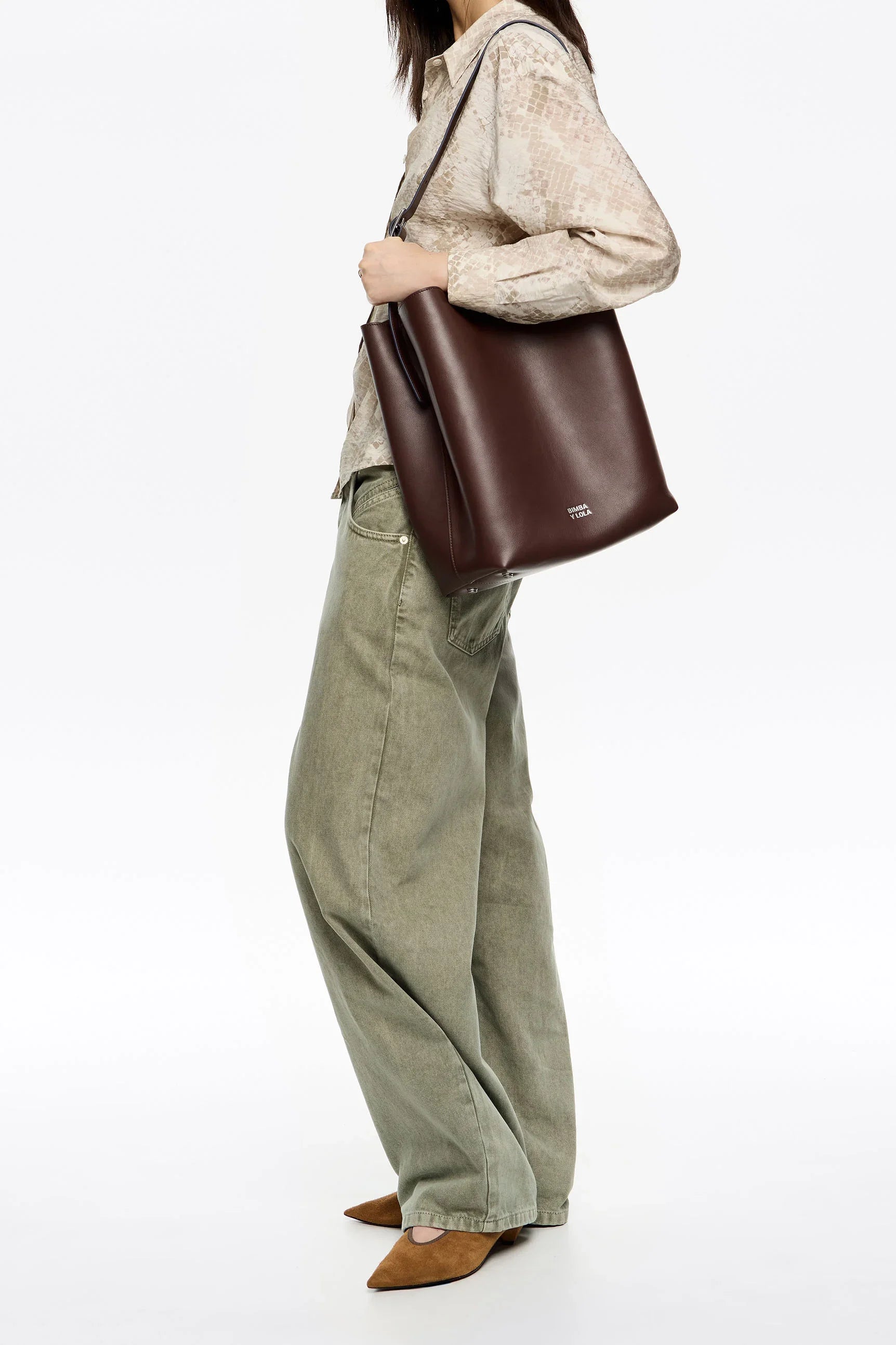 אישה עם תיק כתף עור חום גדול, חולצה בהירה ומכנסי ג'ינס רחבים, אופנה יוקרתית ב-CHOZEN