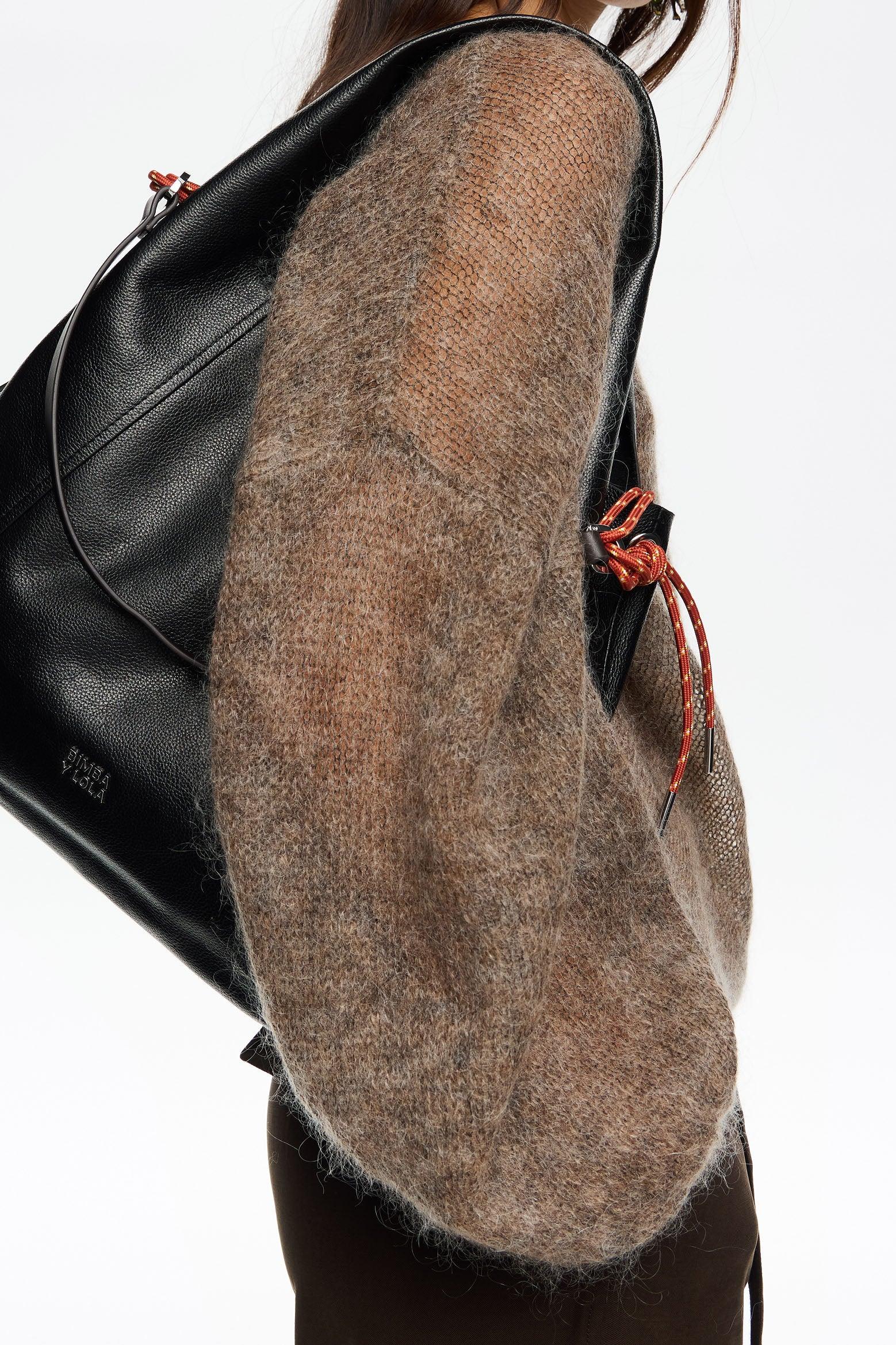 אישה עם סוודר חום נושאת תיק גב שחור מעור, מותג CHOZEN אופנה יוקרתית