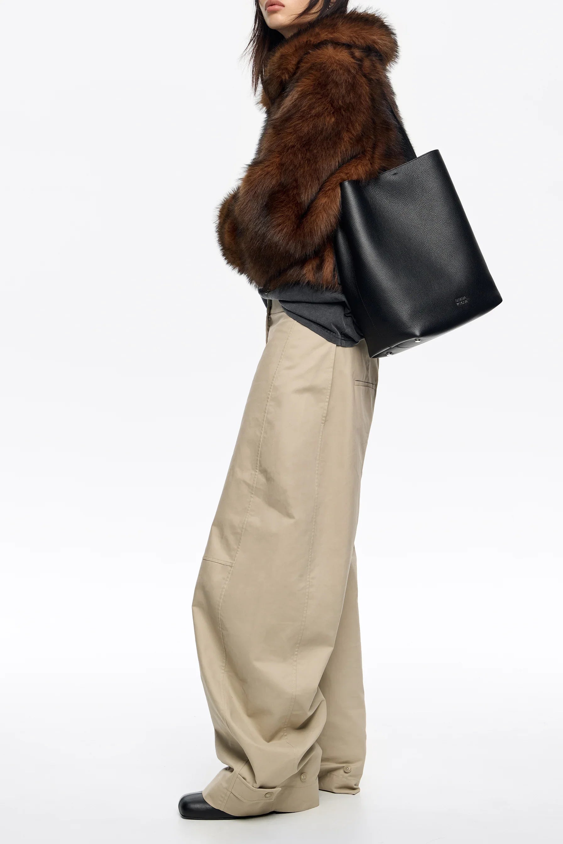 אישה עם מעיל פרווה חום, תיק עור שחור ומכנסיים בז' רחבים, אופנה יוקרתית CHOZEN