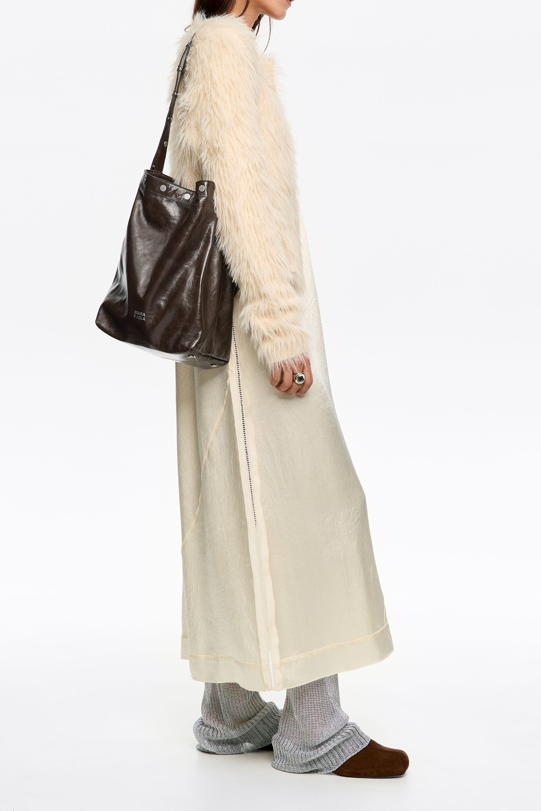 אישה עם מעיל פרוותי, שמלה בהירה, תיק עור חום ונעלי בית אפורות, אופנת CHOZEN