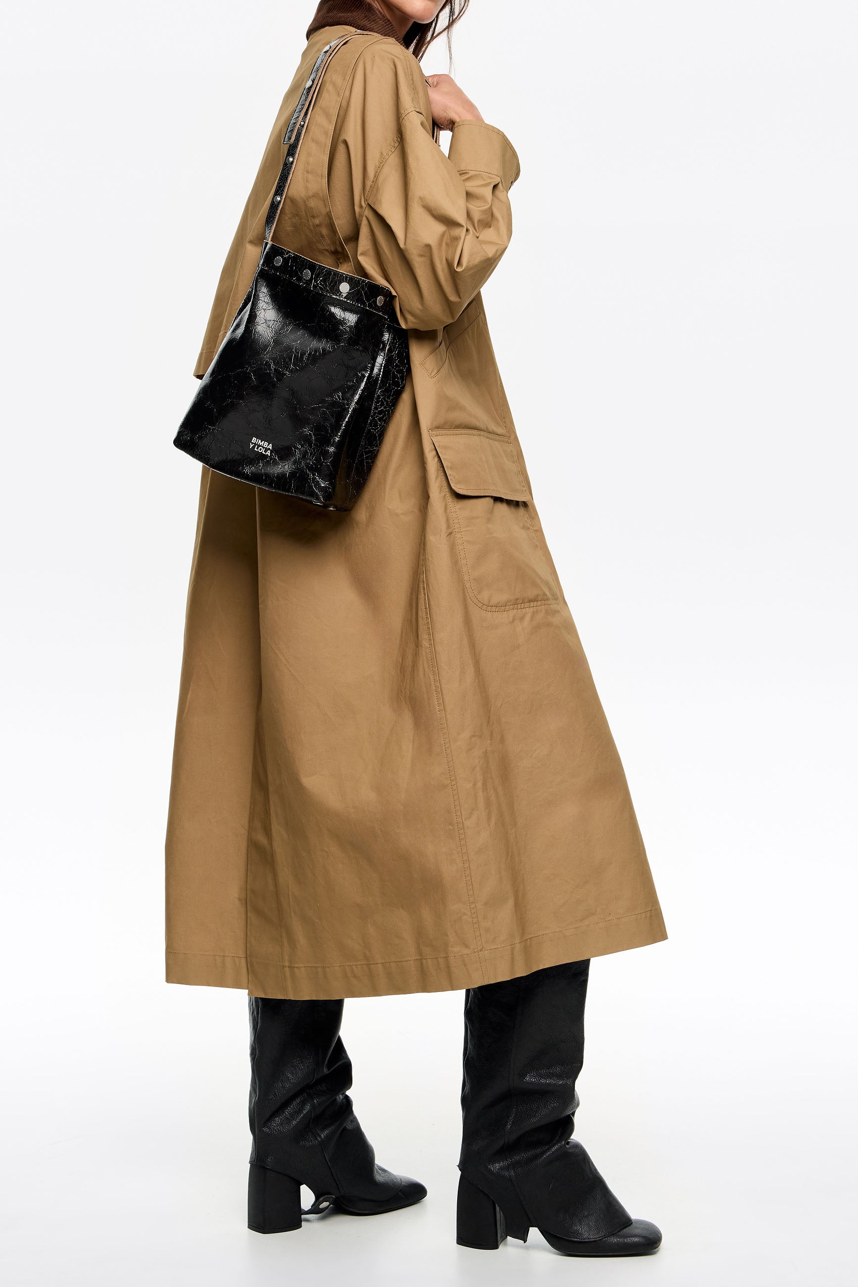 אישה במעיל חום עם תיק עור שחור של מותג יוקרתי ונעליים שחורות, אופנה CHOZEN