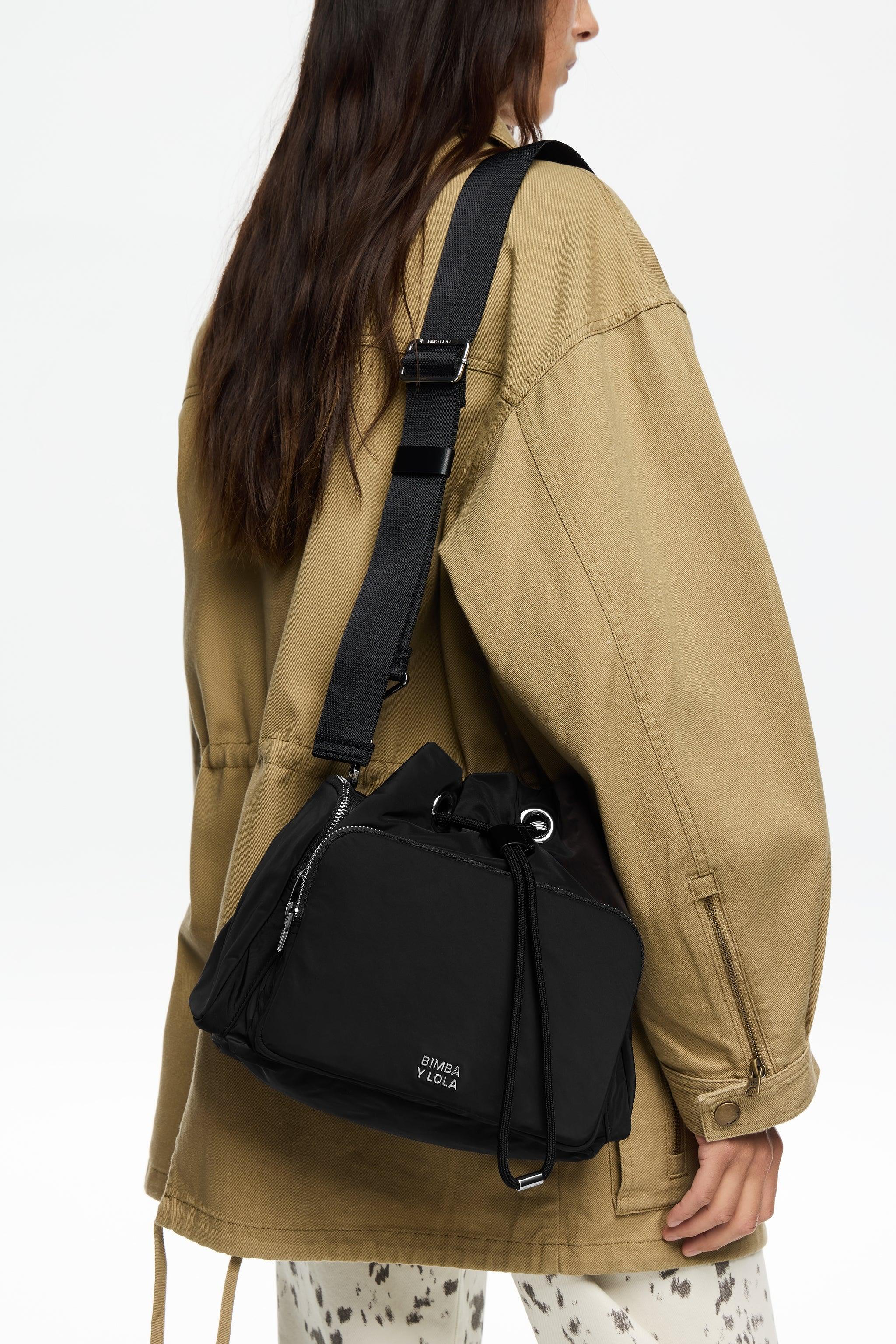 אישה עם תיק שחור של BIMBA Y LOLA, לובשת ג'קט בז', אופנה מעוצבת בחנות CHOZEN