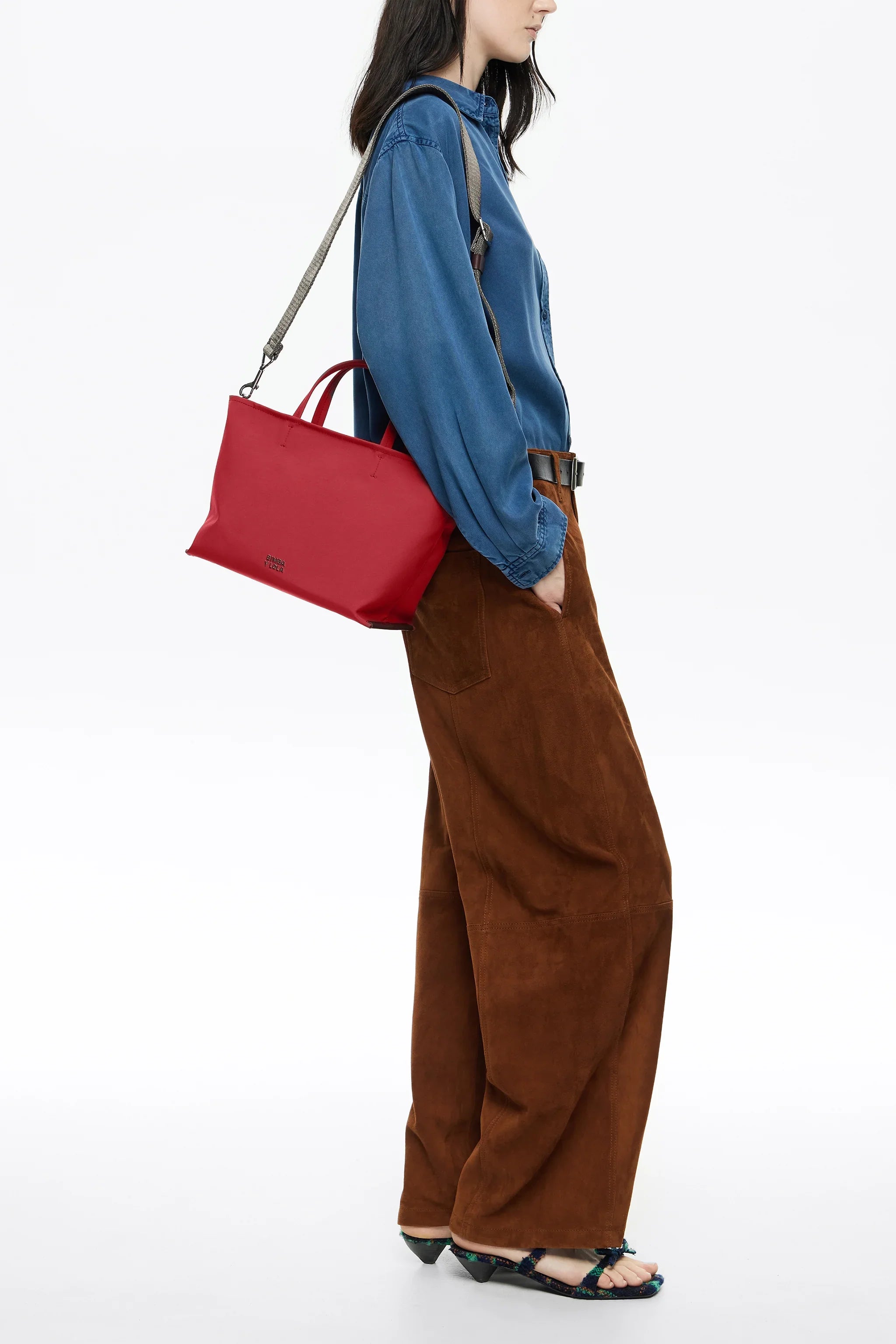 אישה עם חולצת ג'ינס כחולה ומכנסיים חומים נושאת תיק אדום של מותג CHOZEN