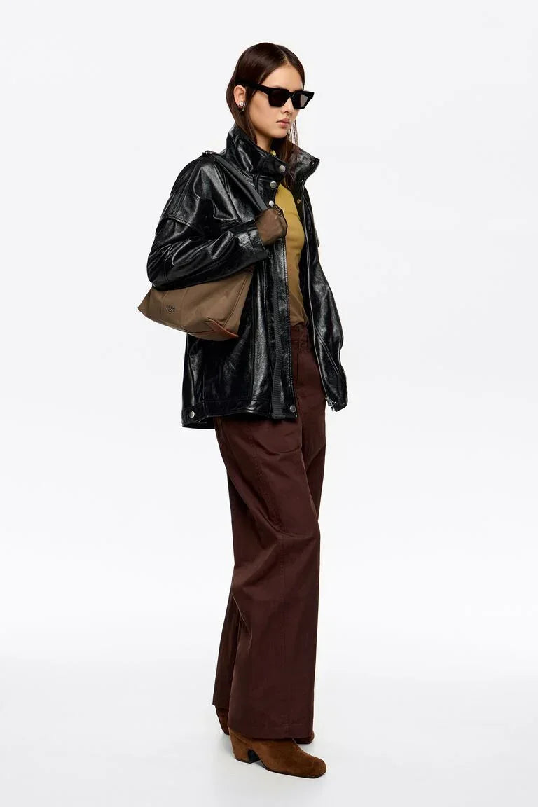 אישה עם מעיל עור שחור, מכנסיים חומים, משקפי שמש ותיק אופנתי, צילום אופנה CHOZEN