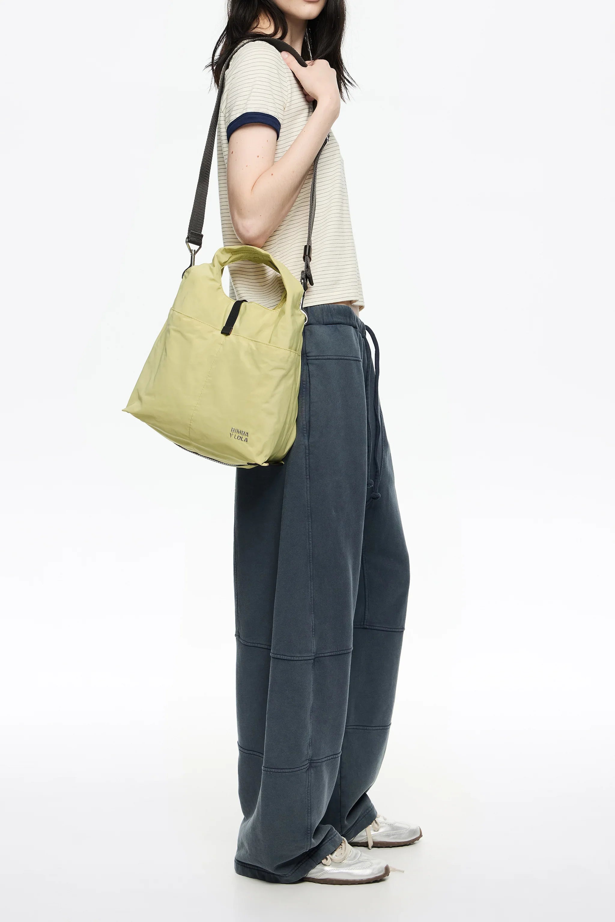 אישה עם תיק יד ירוק של BIMBA Y LOLA, לובשת חולצה מפוספסת ומכנסיים רחבים, אופנה עכשווית מבית CHOZEN