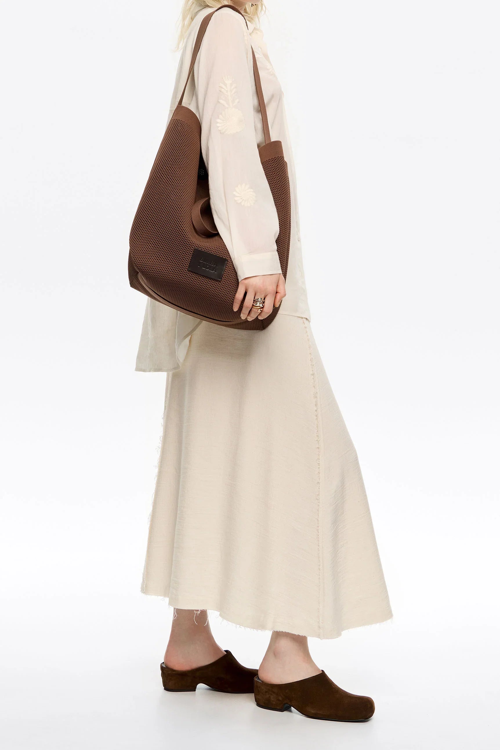 אישה עם תיק חום אופנתי, שמלה שמנת ונעלי עקב חומות מציגה פריט מעוצב ב-CHOZEN