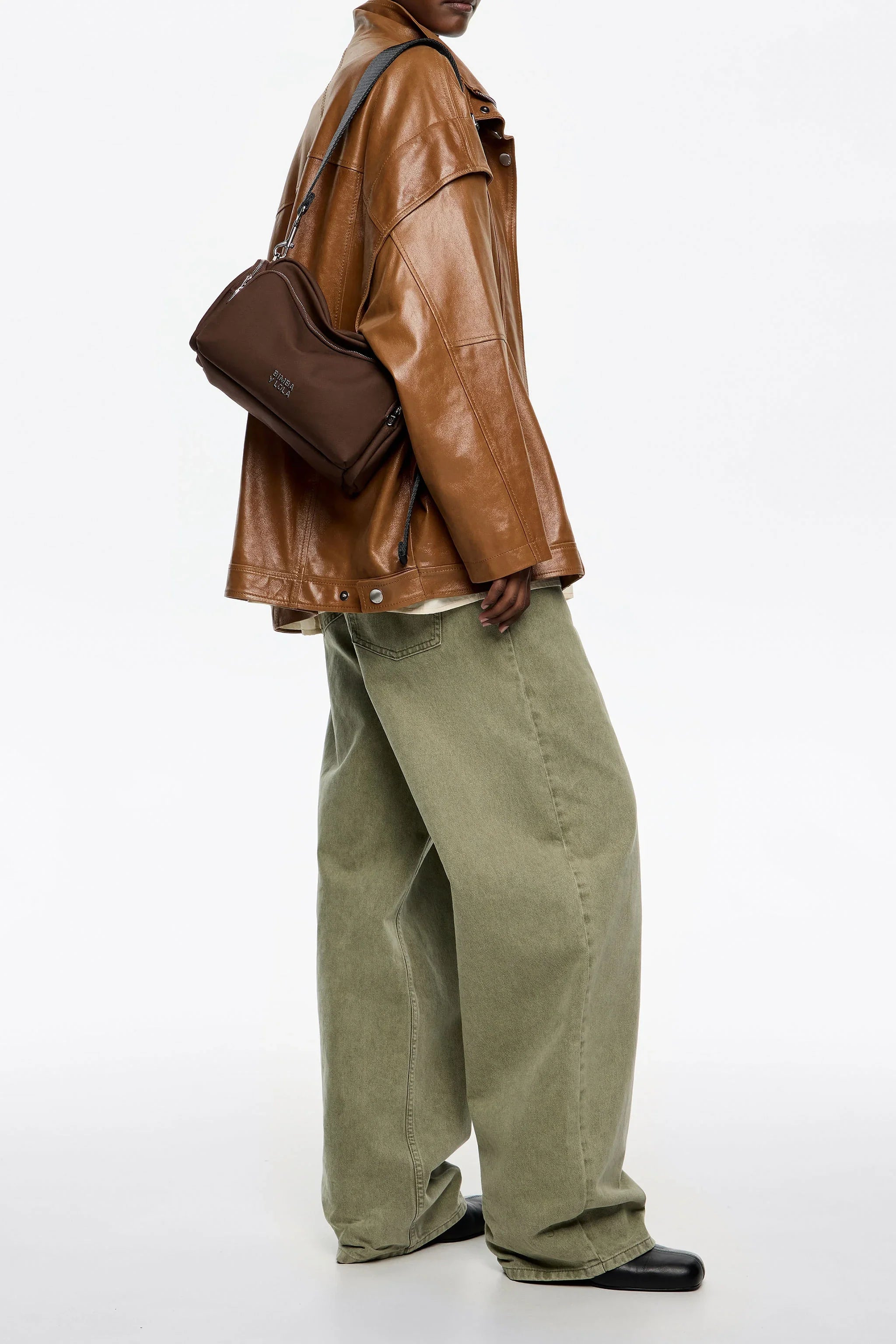 אופנת CHOZEN: דוגמנית עם מעיל עור חום, תיק צד חום ומכנסיים ירוקים רחבים