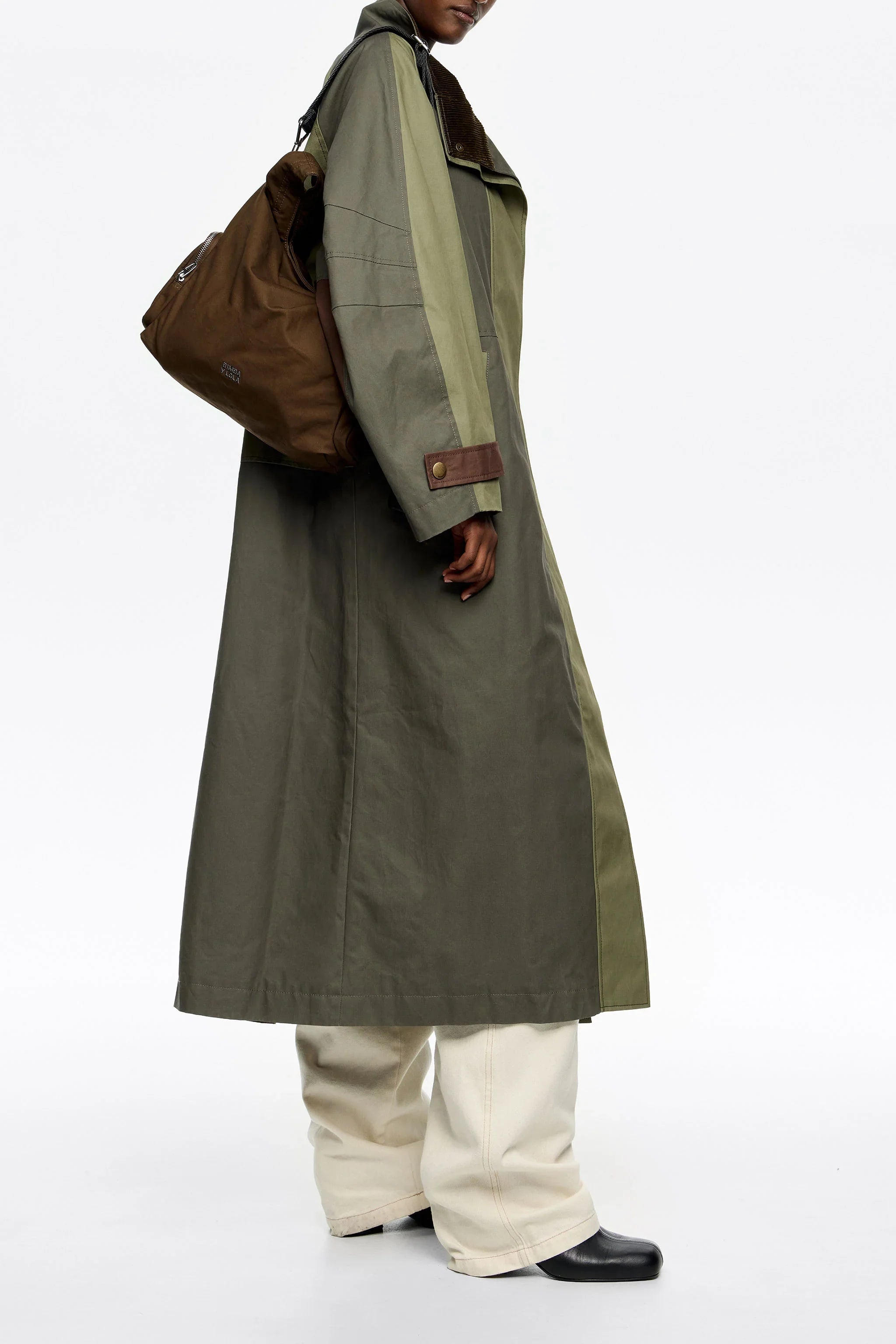 מעיל טרנץ' ירוק אופנתי, מכנסיים בהירים ותיק כתף חום, צילום ל-CHOZEN מותגים מובילים