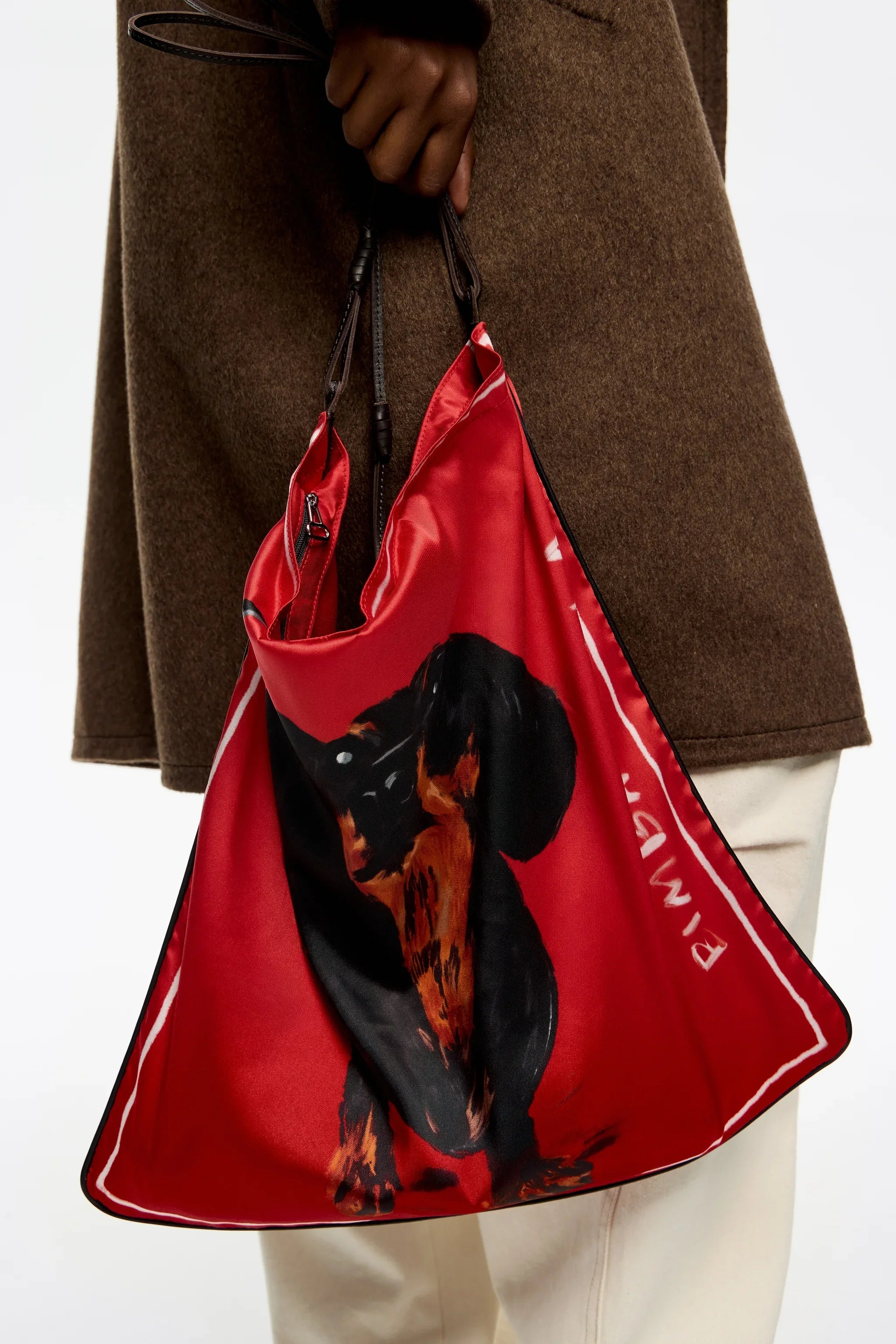 תיק אדום עם איור כלב, מבית CHOZEN, מוחזק ביד עם מעיל חום