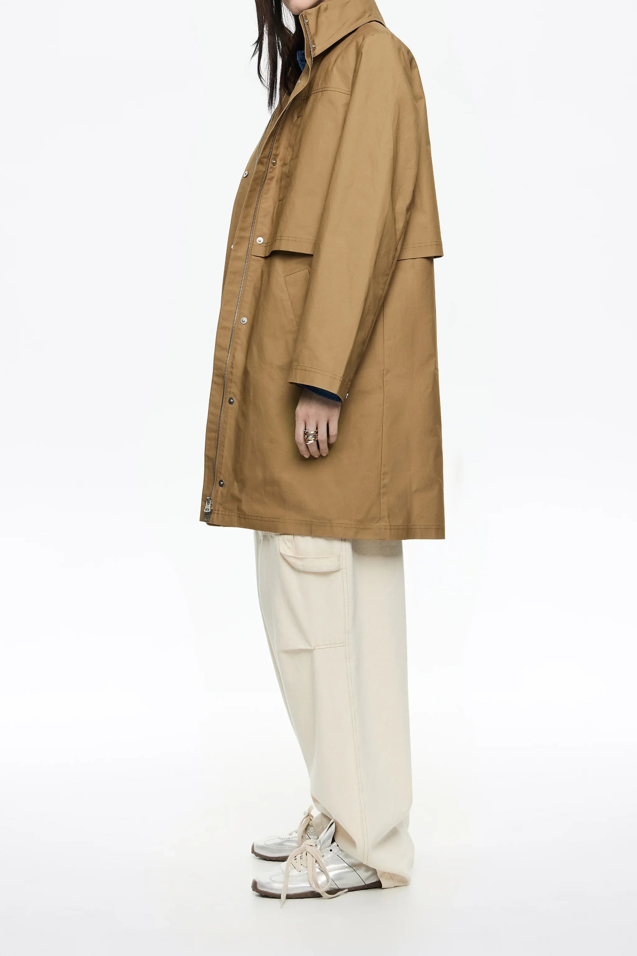 מעיל חום ארוך לנשים של מותג מוביל ב-CHOZEN, על דוגמנית עם מכנסי בז' ונעלי ספורט כסופות