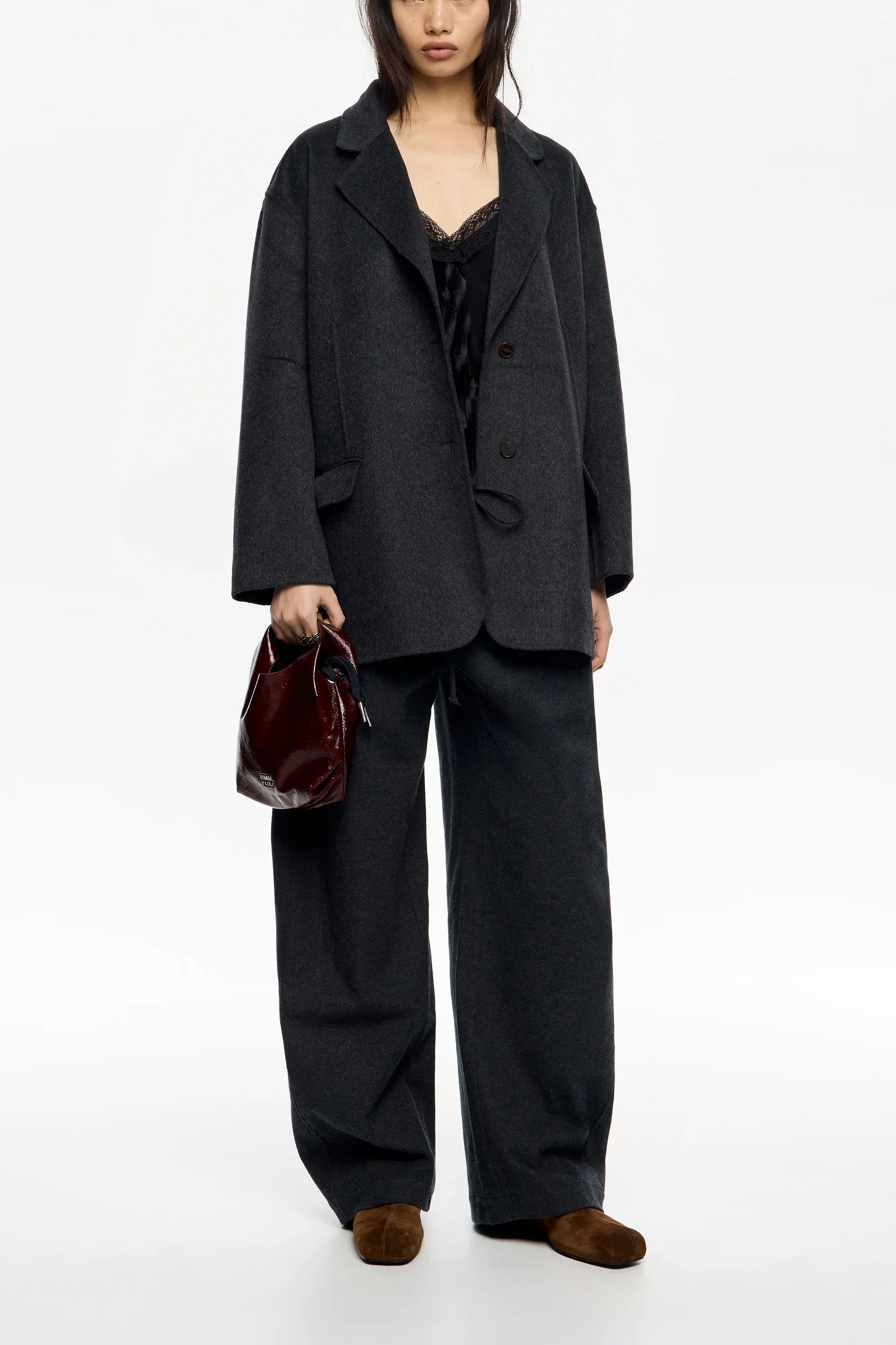 אישה לובשת חליפת מכנסיים רחבה בצבע אפור כהה, מחזיקה תיק בורדו, מותג CHOZEN